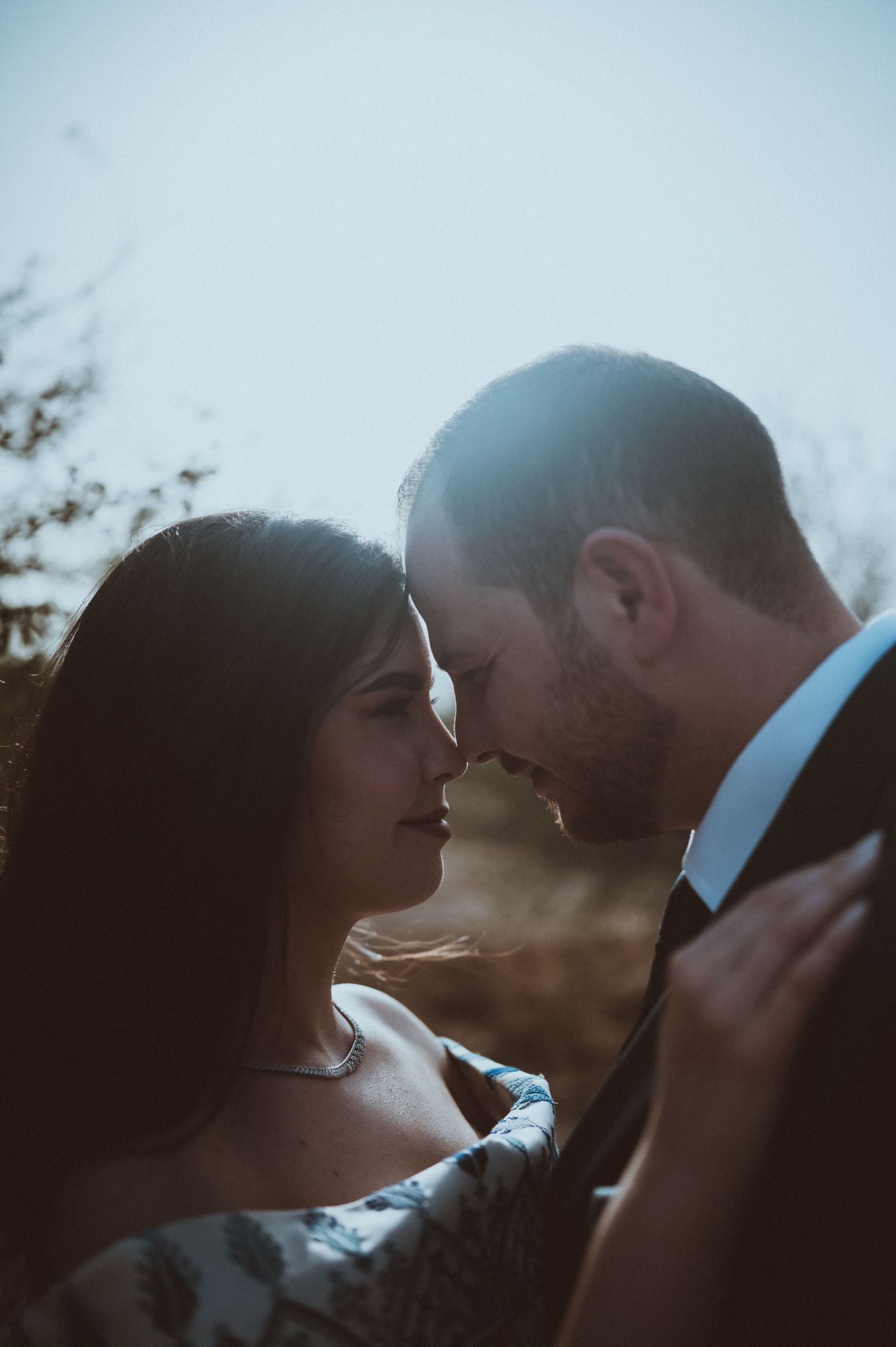 Silhouetted couple sharing an intimate moment against bright sky.