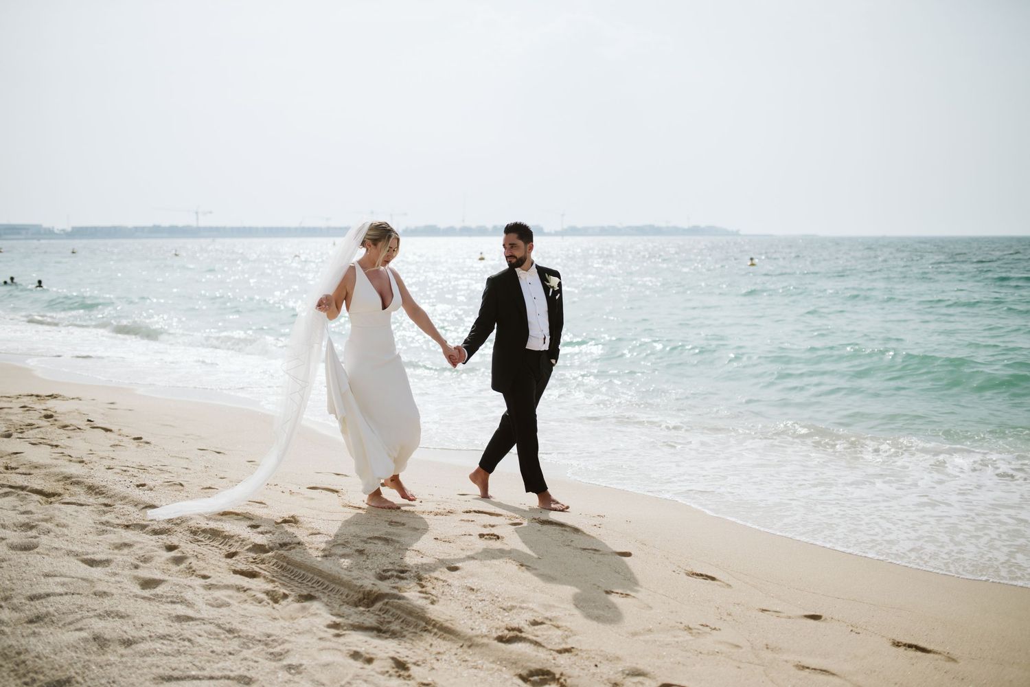 Artistic beach wedding photos with couple walking along shoreline in moody lighting.