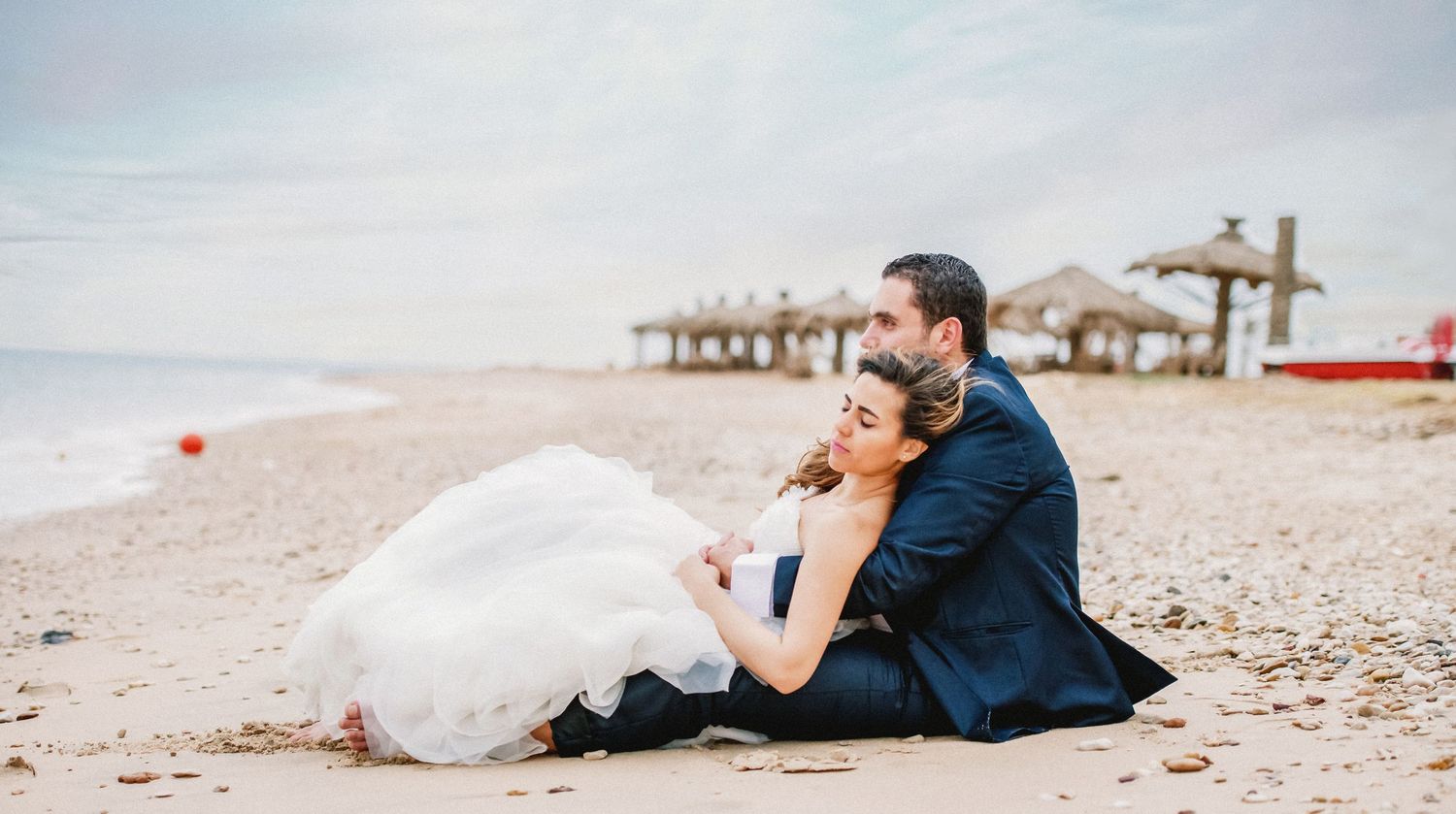 Couple relaxes together on beach with umbrellas and palm trees in background.
