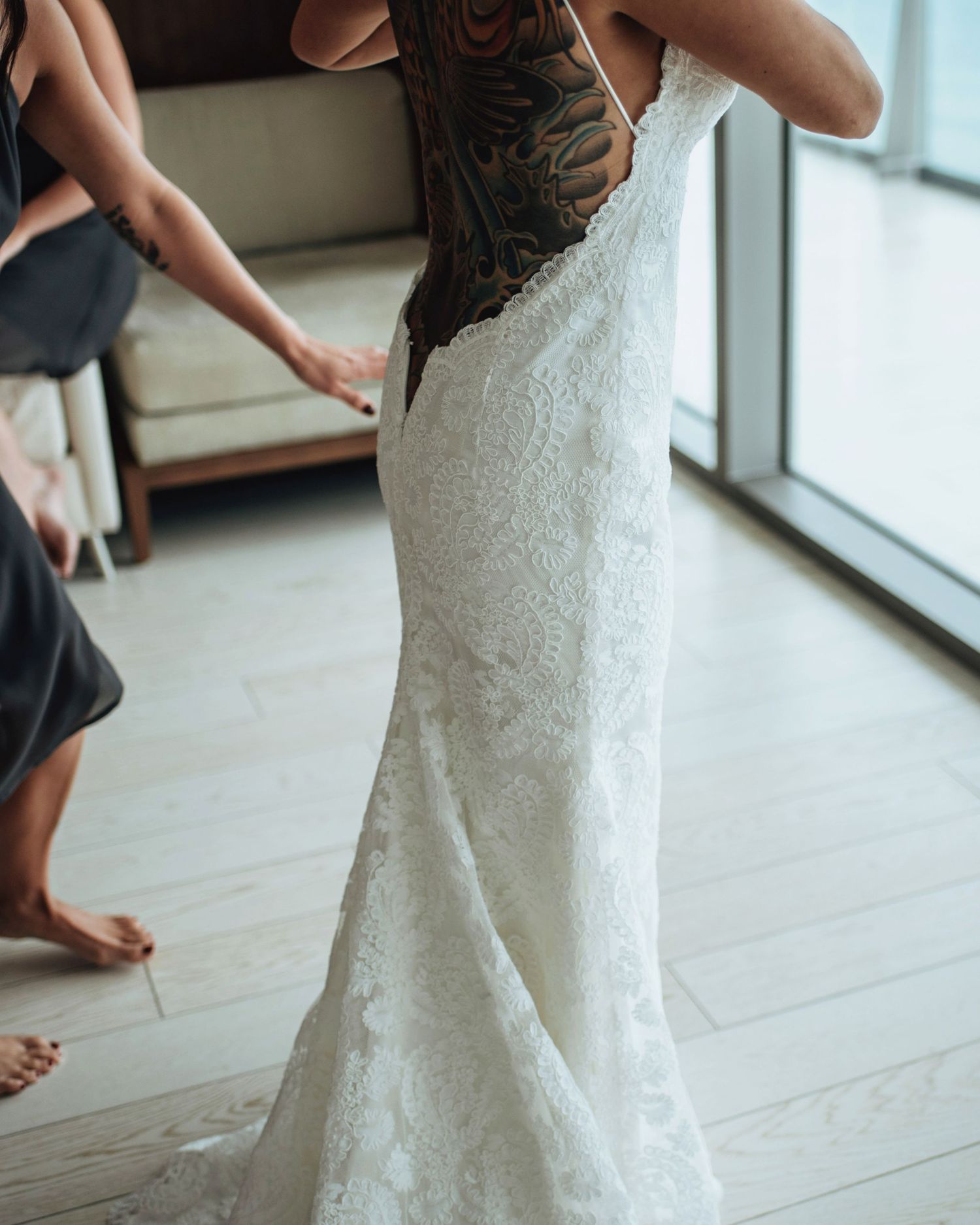 Close-up view of a fitted lace wedding dress being worn in a sunlit room.