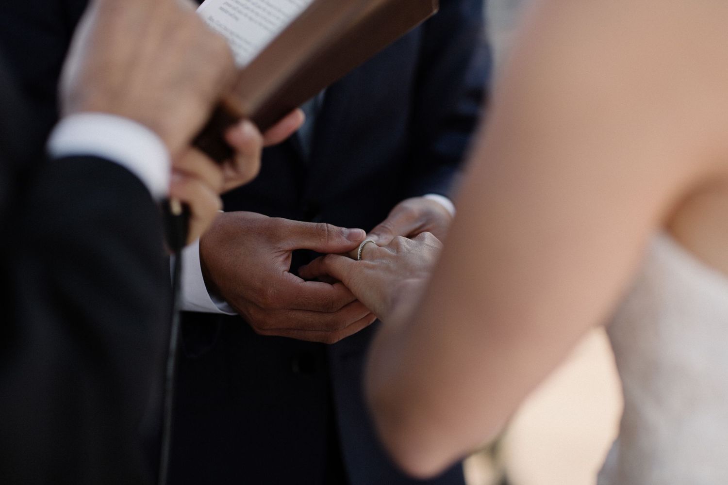 Close-up details of wedding ceremony moments showing hands and formal attire.