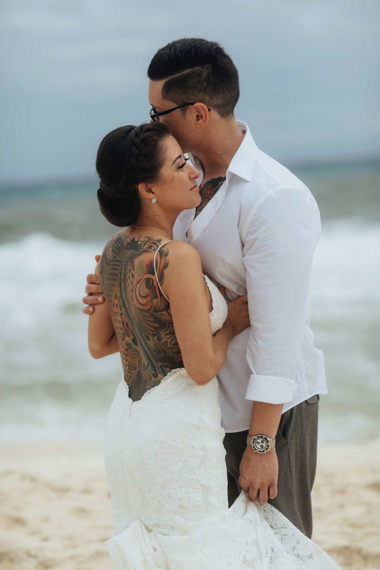 Beach wedding photography showing tattoo details and intimate embrace.