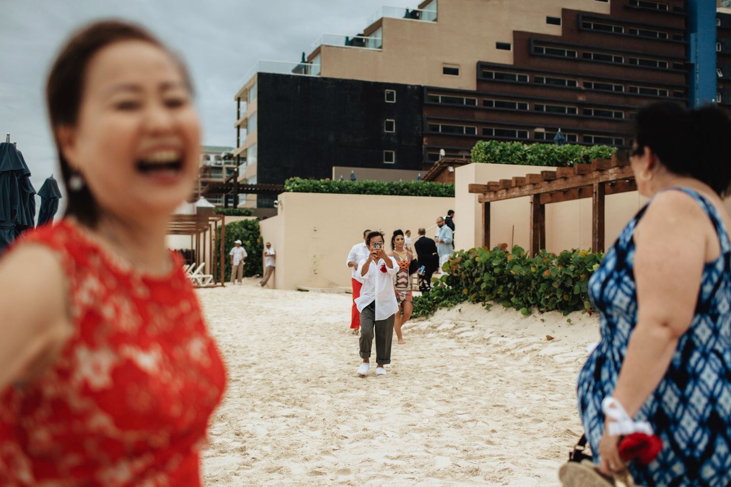 Wedding guests celebrating joyfully on a sandy beach with resort buildings visible.
