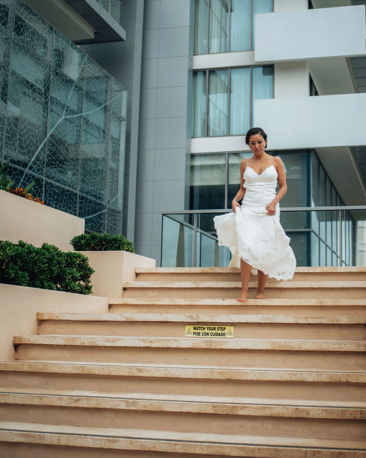 A person in a wedding dress descending concrete stairs outside a modern building.