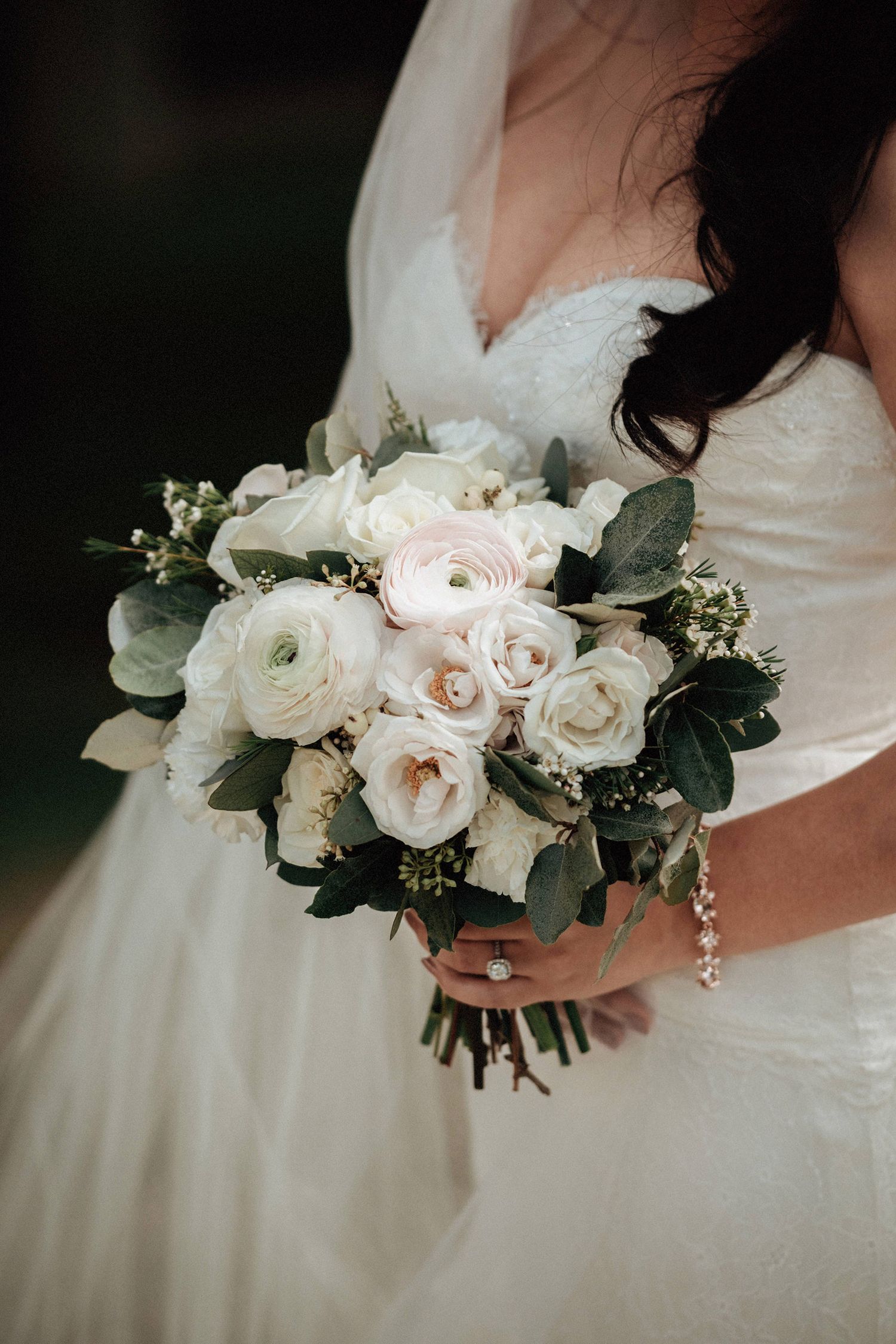 Elegant white and blush rose wedding bouquet with eucalyptus leaves against a white dress.