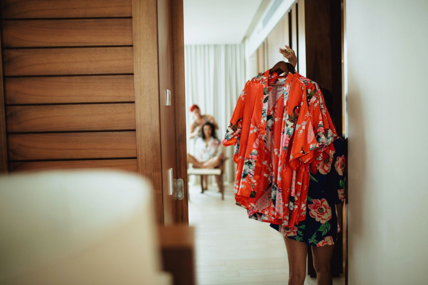 Person wearing vibrant red floral robe walking through doorway in hotel hallway.