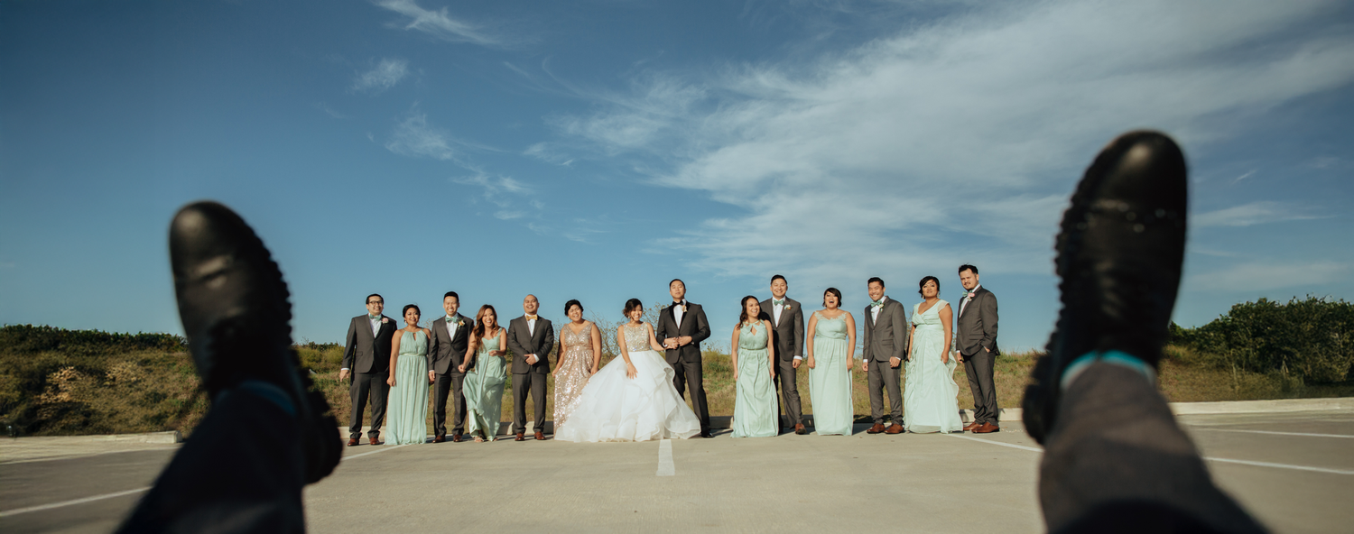 Wedding party stands together on scenic beach with dramatic cloudy sky.