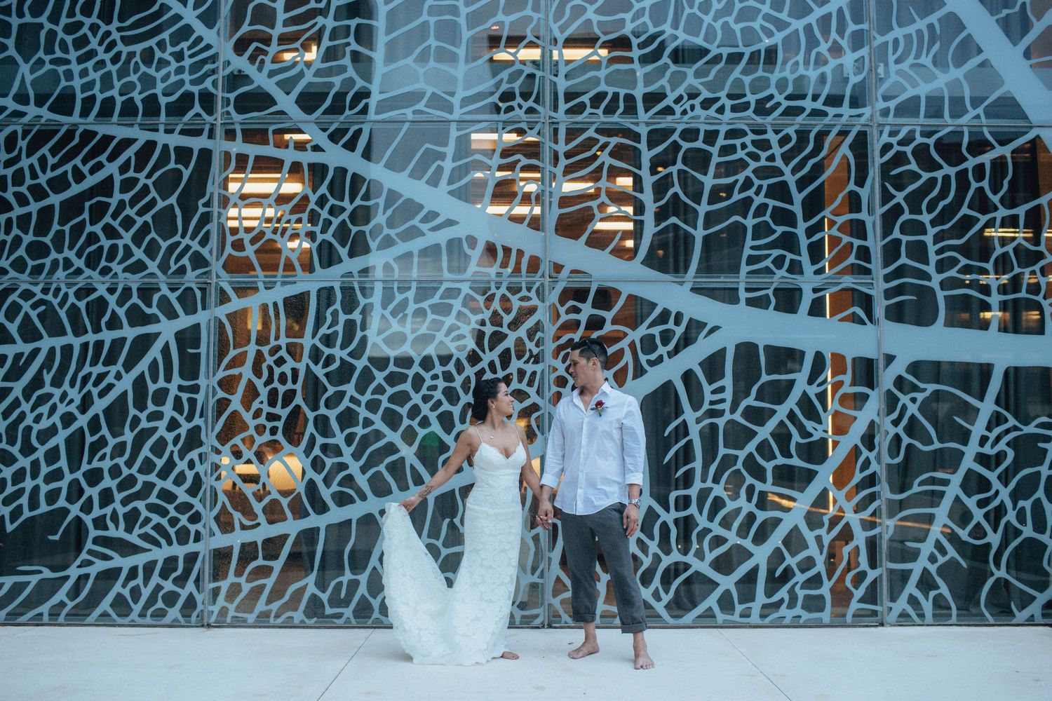 A couple poses in front of a modern geometric blue wall design at night.