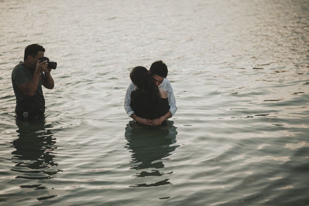 Photographers wading in water while taking pictures at sunset. Jojo Pangilinan Photographers, Dallas based Destination wedding photographer