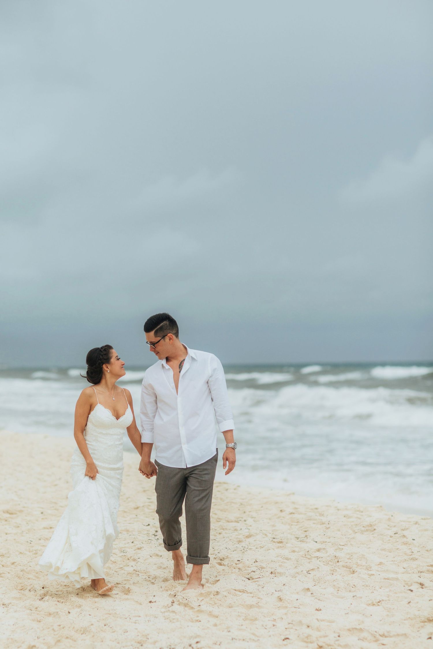 Couple walking and playing together on a scenic beach with crashing waves in the background.