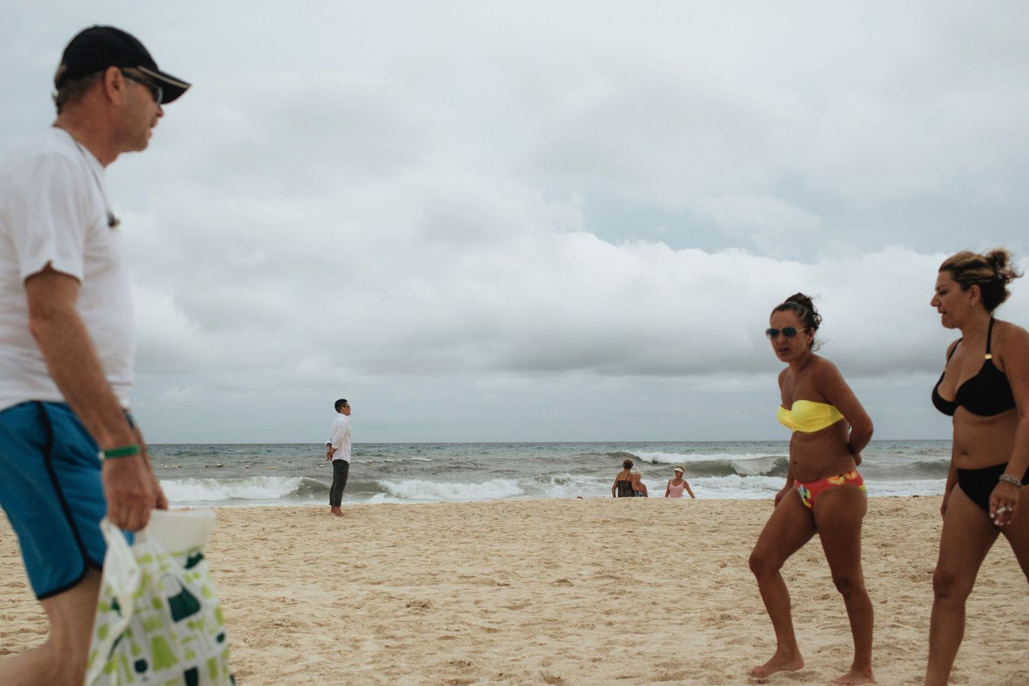 People enjoying a cloudy day at the beach with waves in the background.