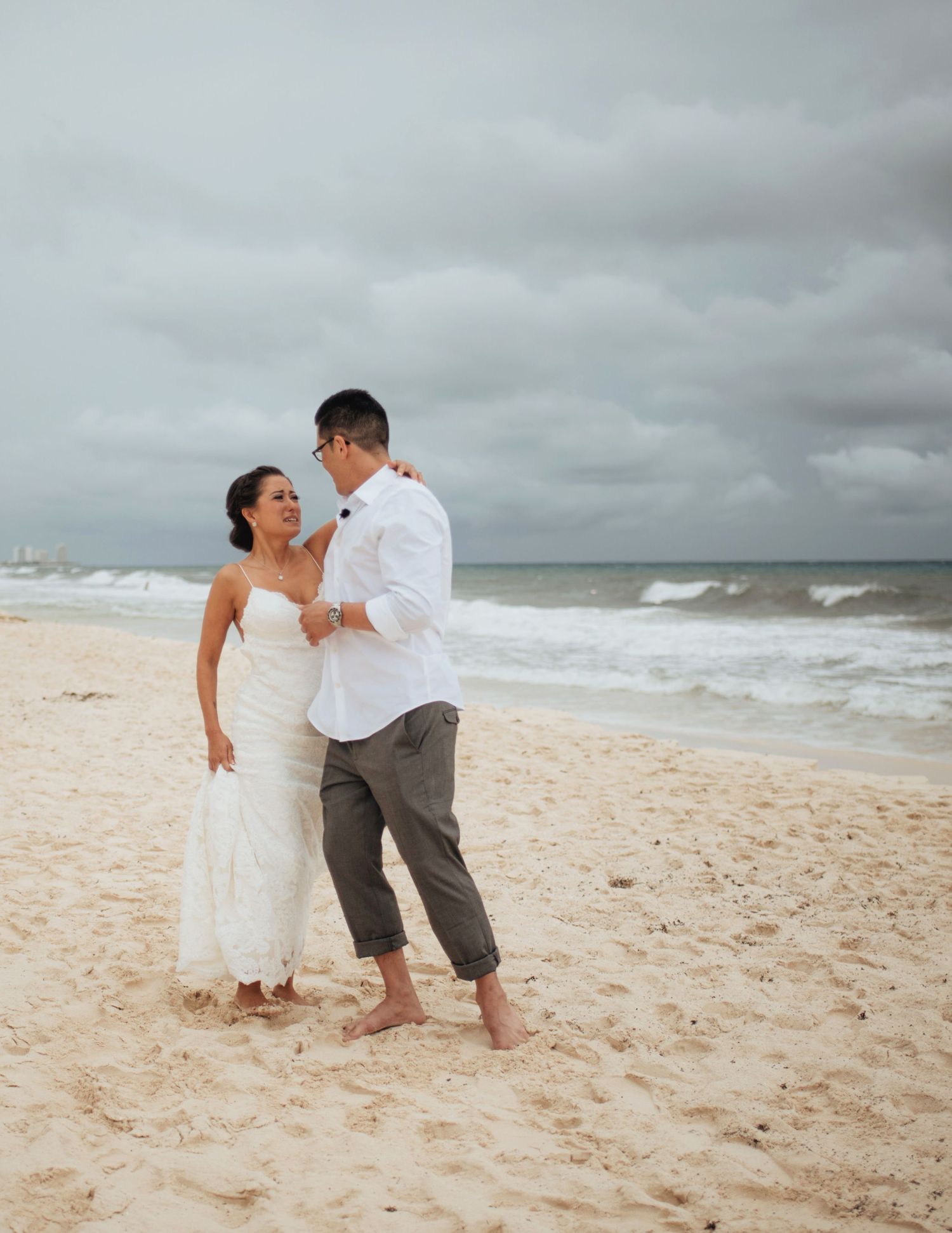 Couple playfully poses together on a sandy beach with stormy skies overhead.