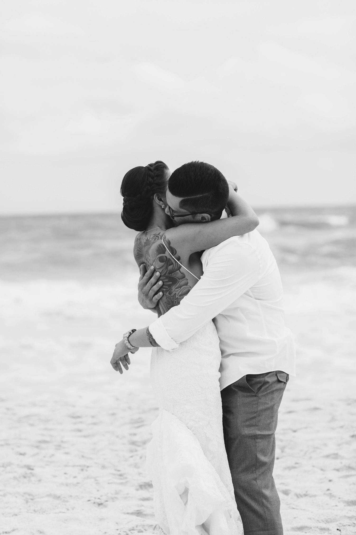 Black and white photo of a loving embrace on a windswept beach.