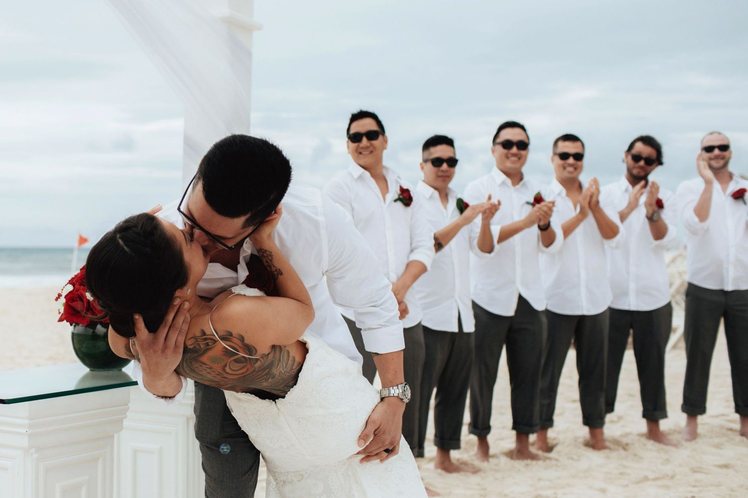 Wedding party lined up on beach with groomsmen in white shirts and dark pants.