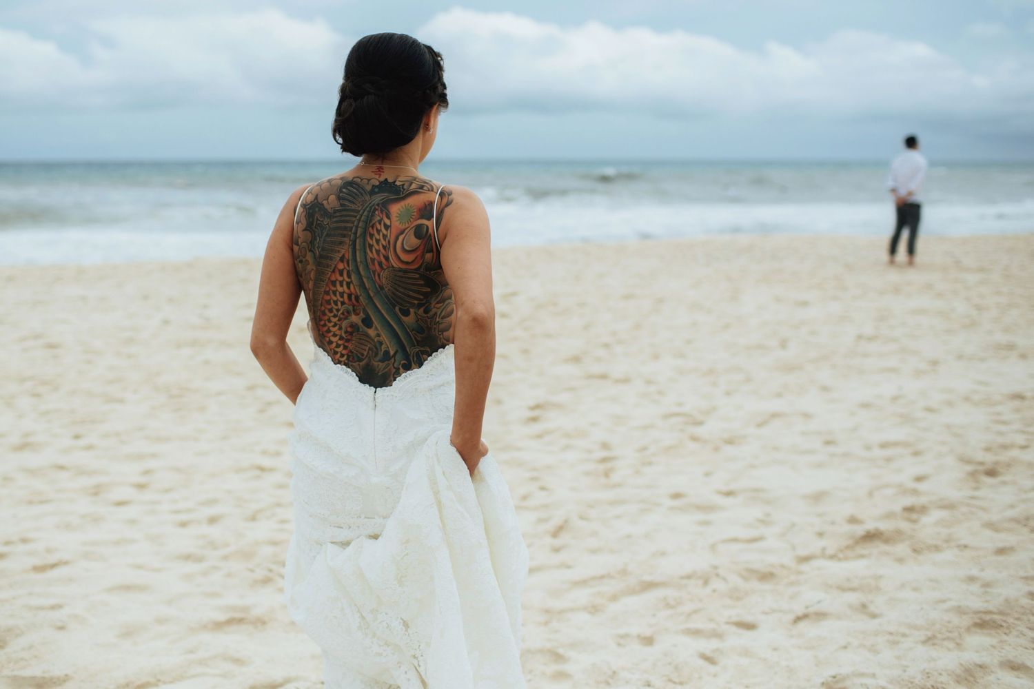 A couple embraces on a cloudy beach with waves crashing in the background.