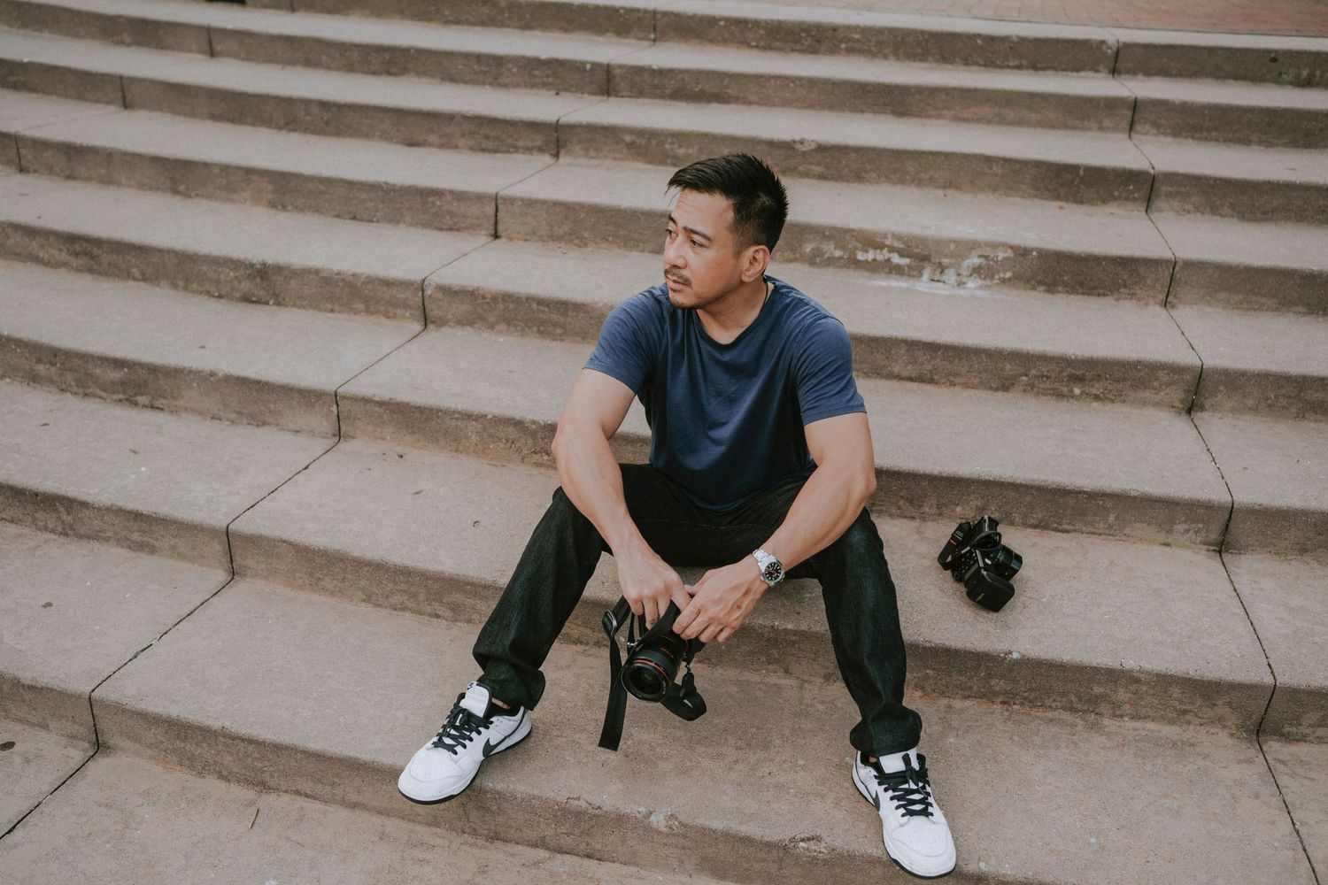 Person sitting casually on concrete steps wearing casual attire and sneakers.