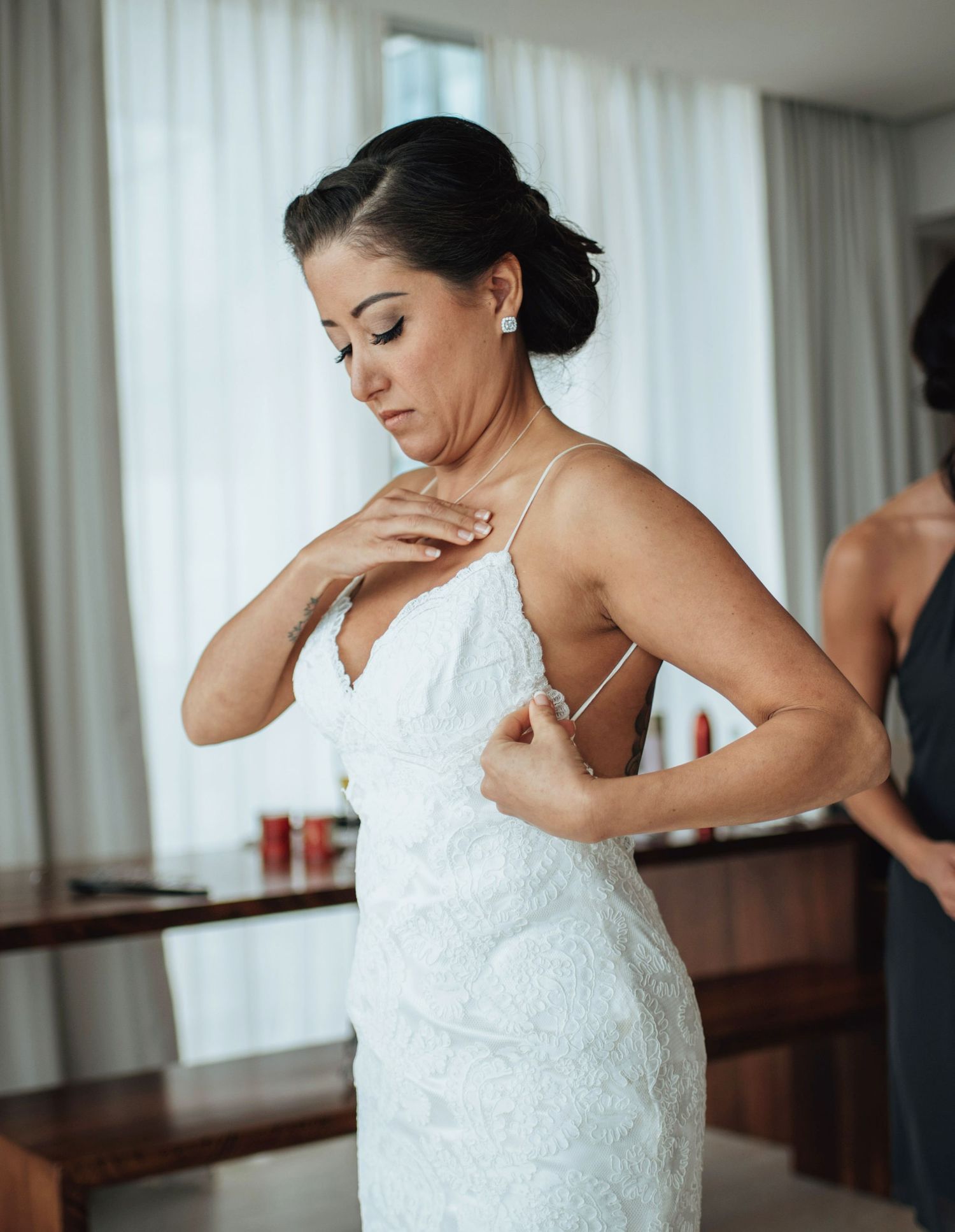 A person in a white lace wedding dress adjusting their gown in a bright room.