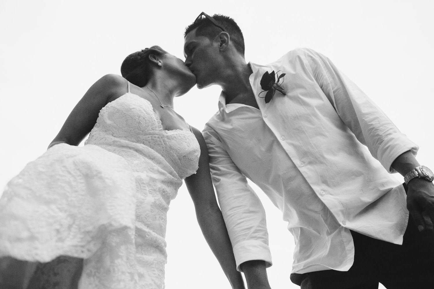A couple in white outfits embraces while dancing on a beach.
