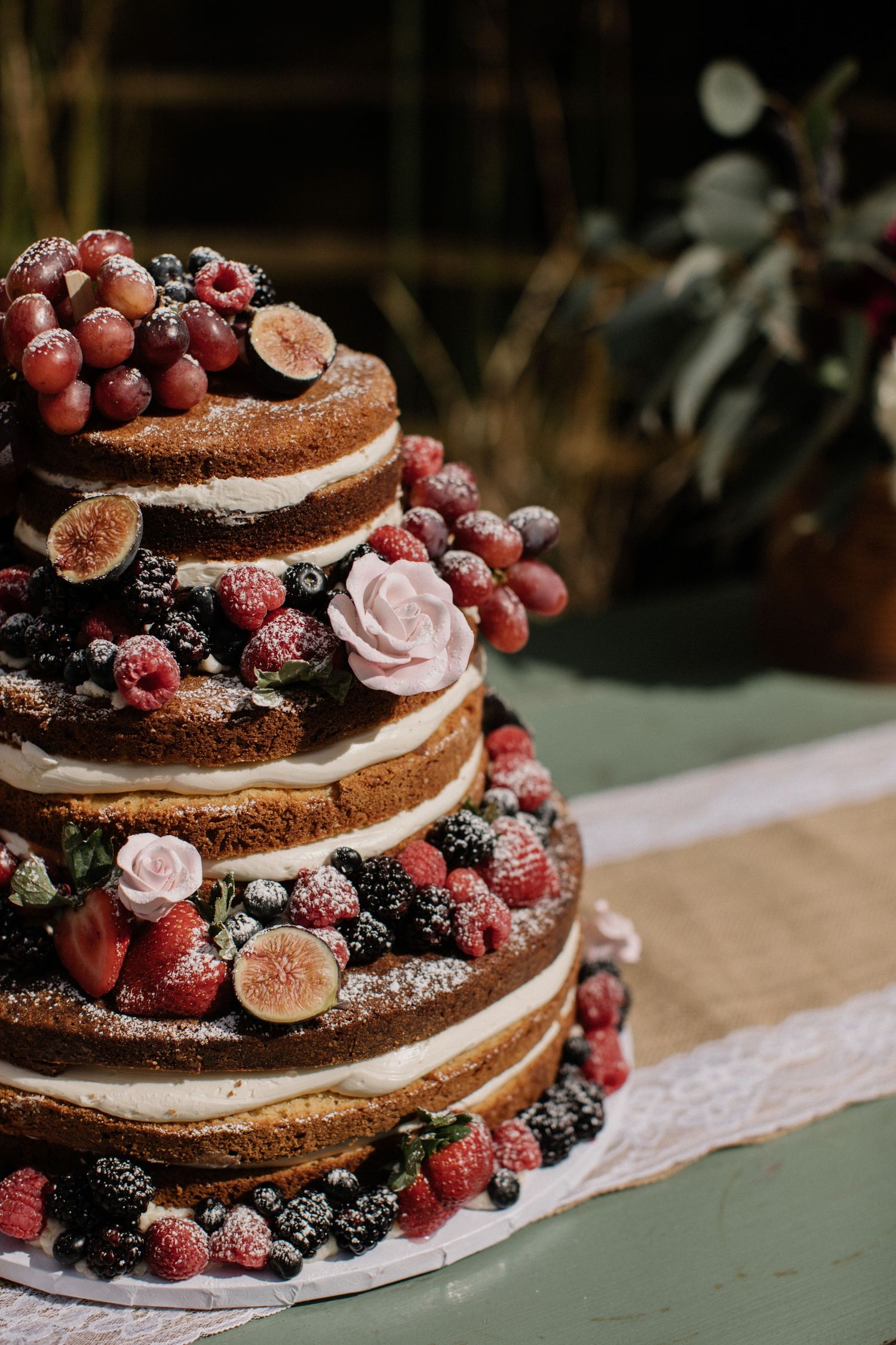Rustic wedding cake decorated with fresh berries, figs and delicate pink roses.