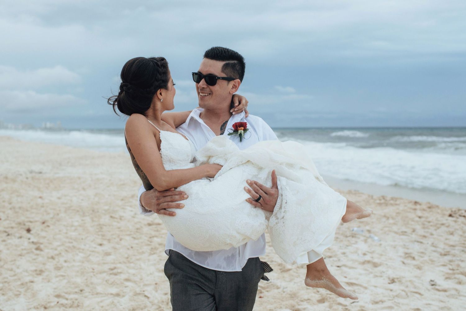 A couple shares a romantic moment on a sunny beach with ocean waves in the background.