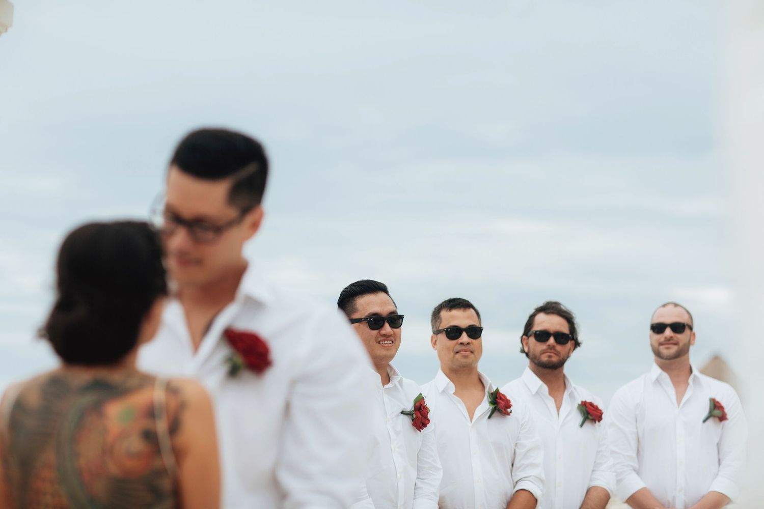 Wedding party in white attire posing together on the beach.