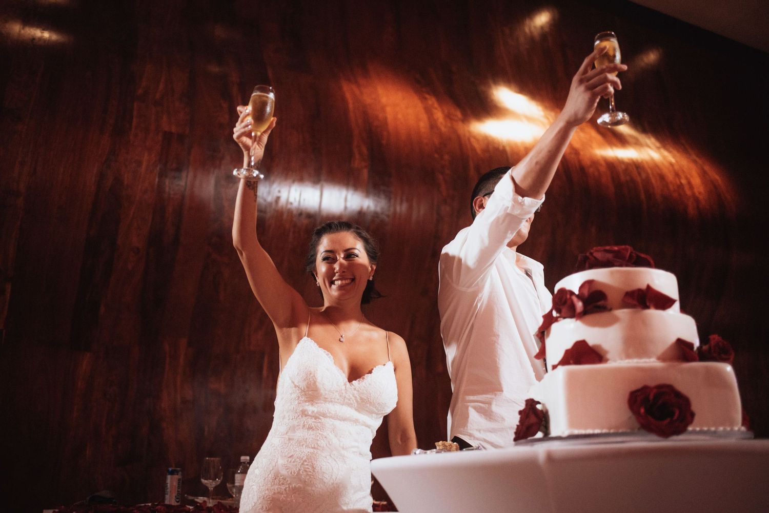 Wedding reception dancers celebrate with raised arms near a white tiered cake.