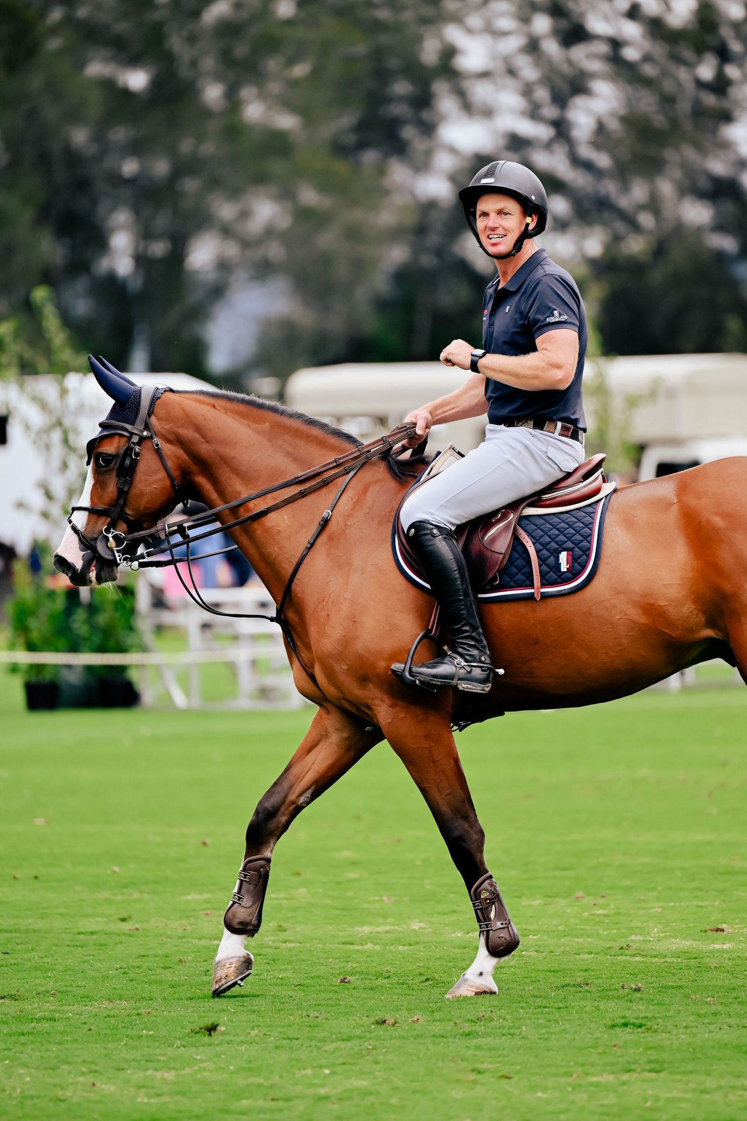 Rider on brown horse galloping across a green polo field during a match.