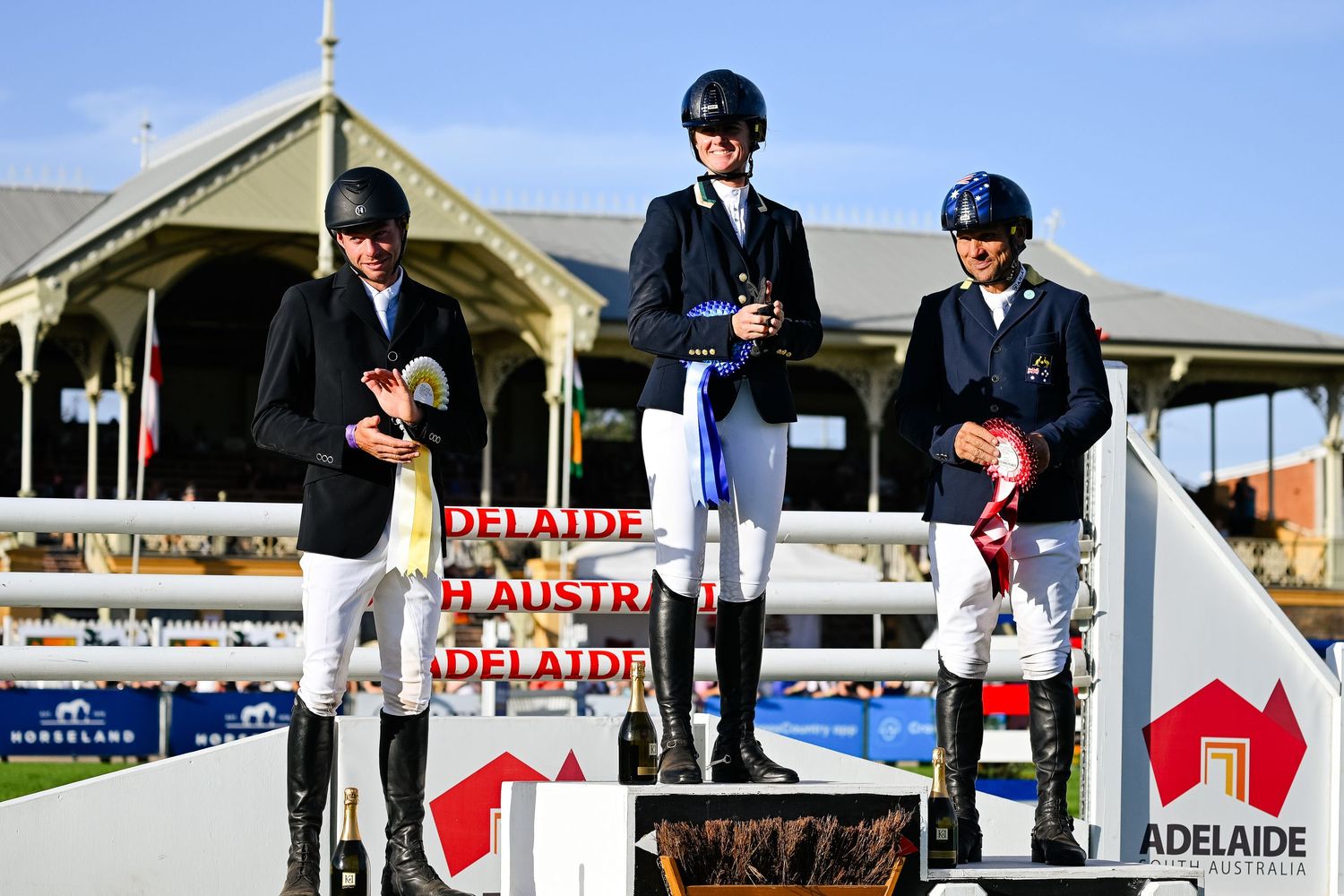 Top placing equestrian event competitors standing atop podium with a competition backdrop.