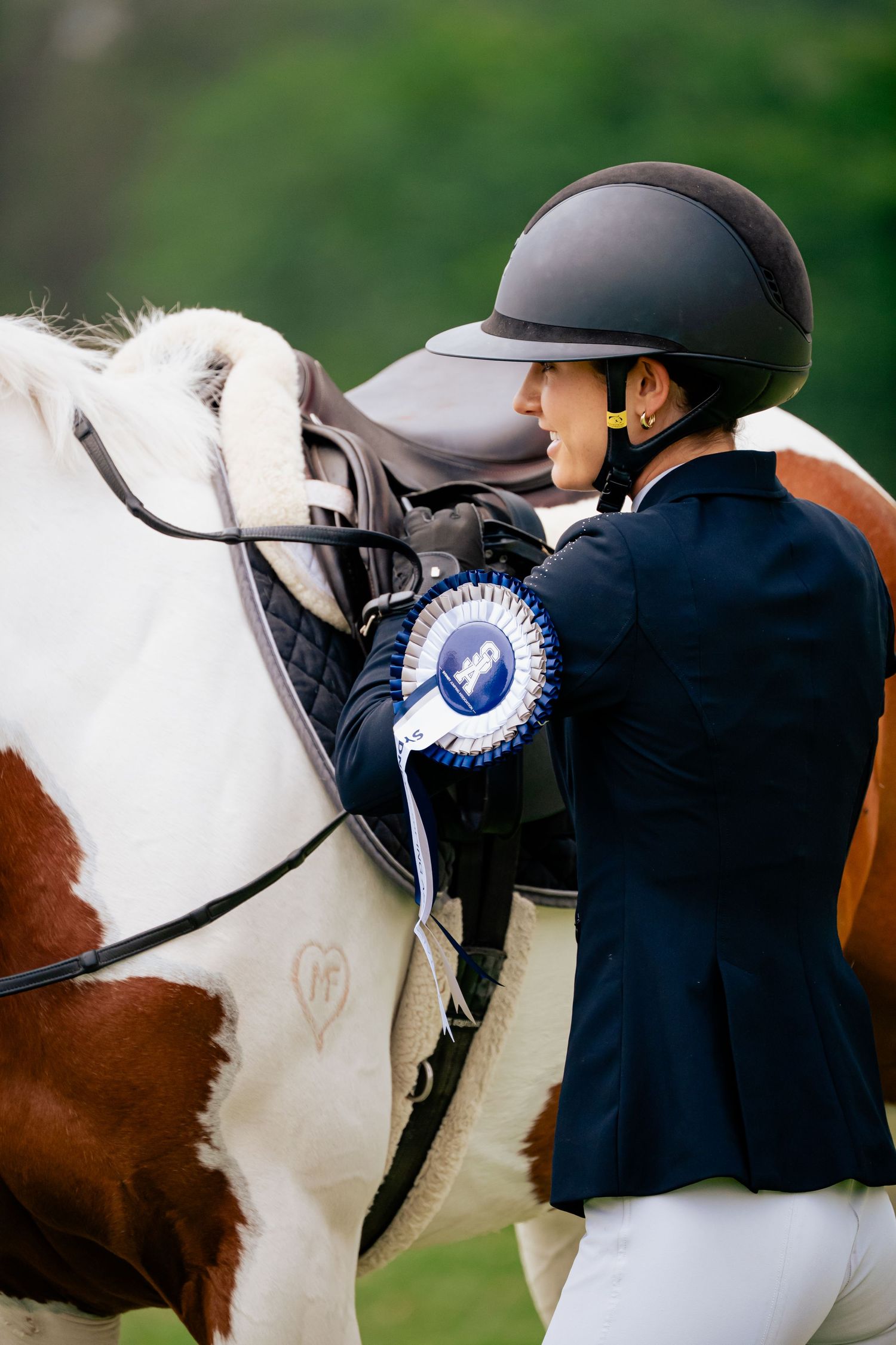 A close-up view of equestrian riders wearing navy jackets and helmets with blue rosettes at a horse show competition.