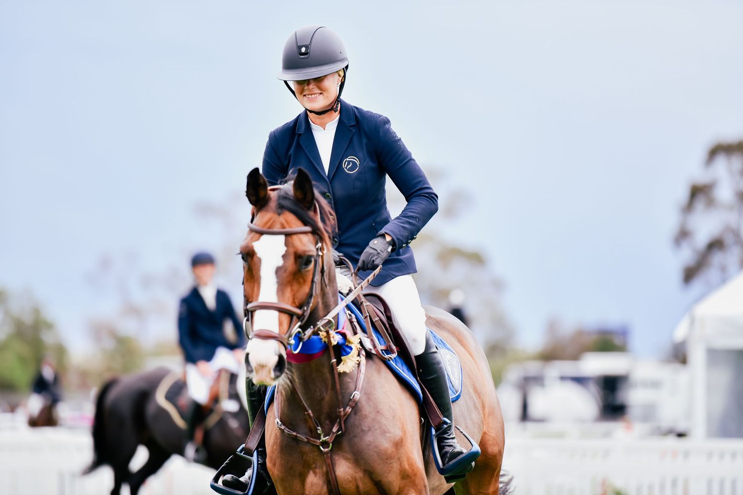 Equestrian riders compete in show jumping competition over colorful obstacles on sandy arena.