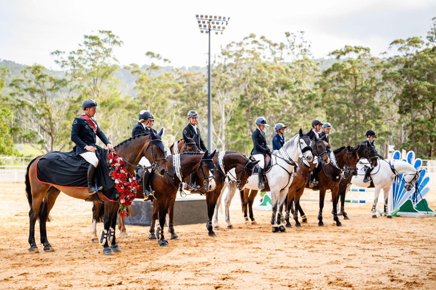 Line of equestrians mounted on horses during an outdoor competition event.
