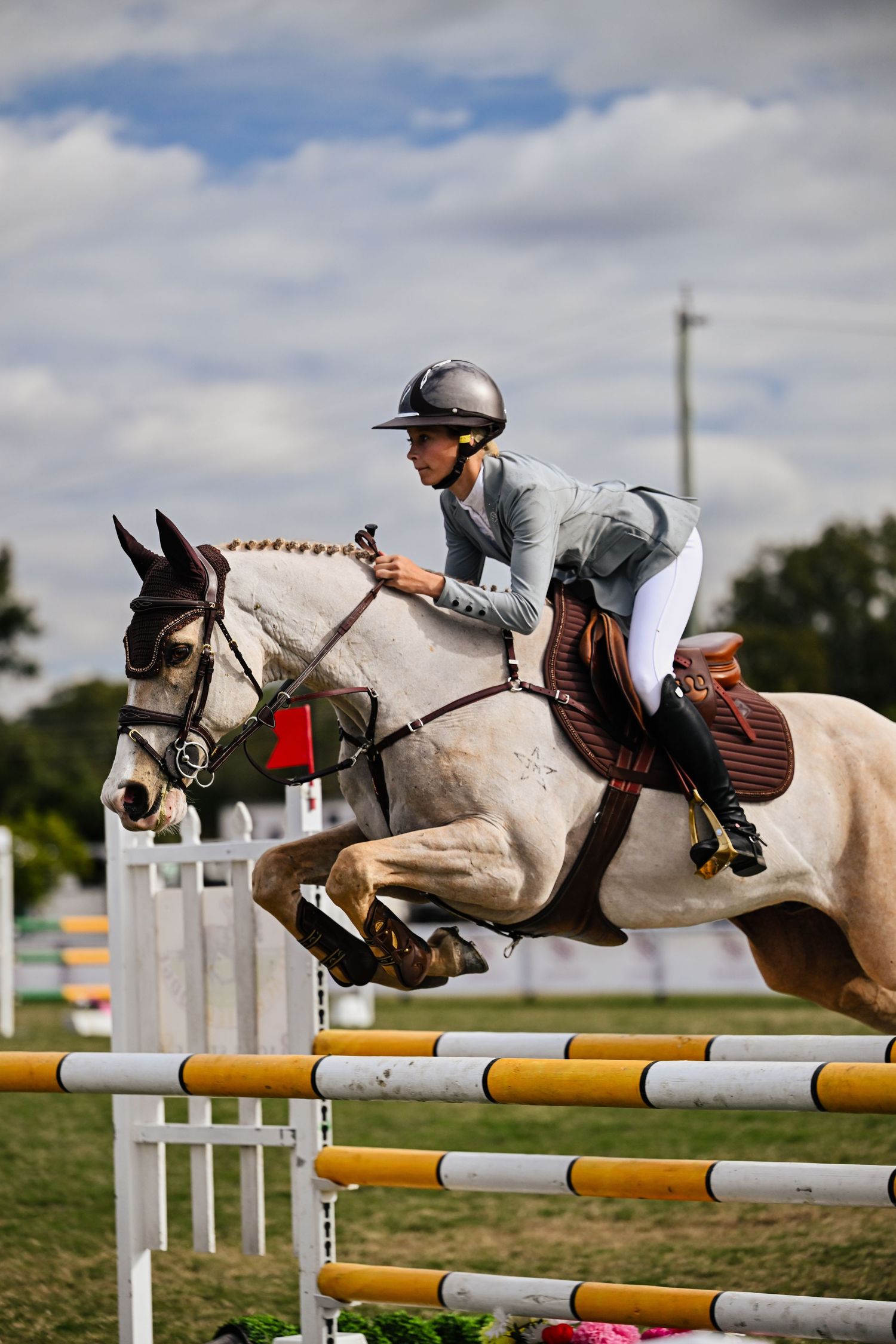 Rider on white horse clearing a show jump on outdoor arena.