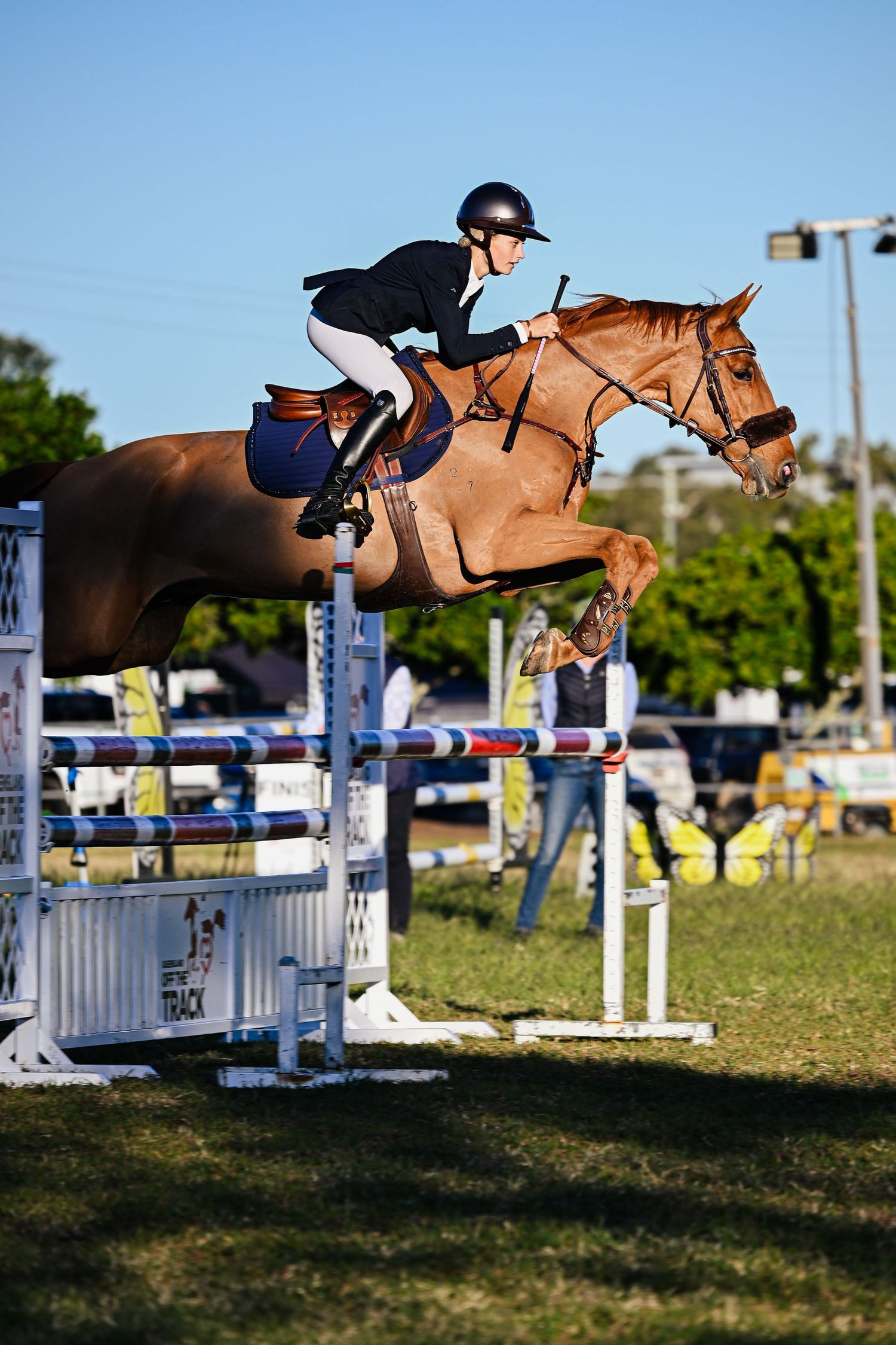 Rider jumping on chestnut horse over a show jump in an outdoor arena.