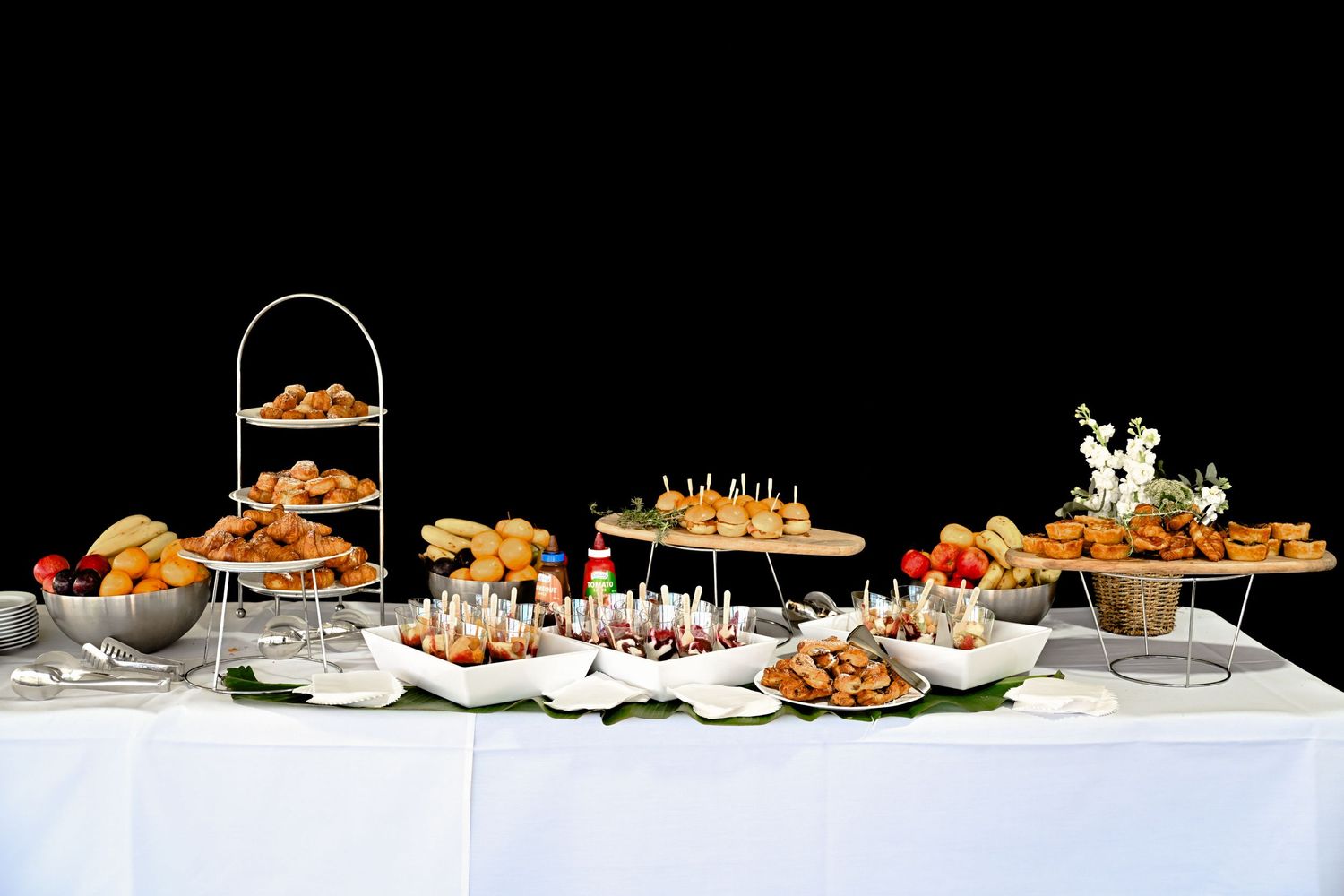 Appetizing array of catering platters filled with finger foods and snacks arranged on a white tablecloth.
