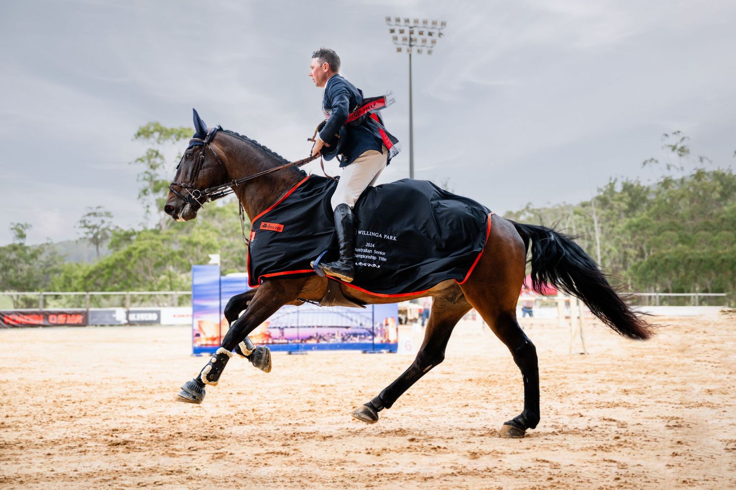 Equestrian athlete and horse clearing jumping obstacle in dramatic action shot.