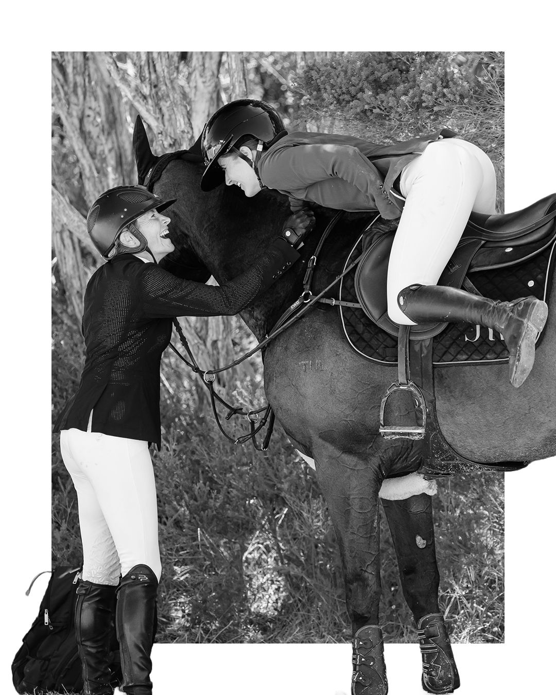 Two equestrians in riding helmets and white breeches assist each other mounting a dark horse outdoors.