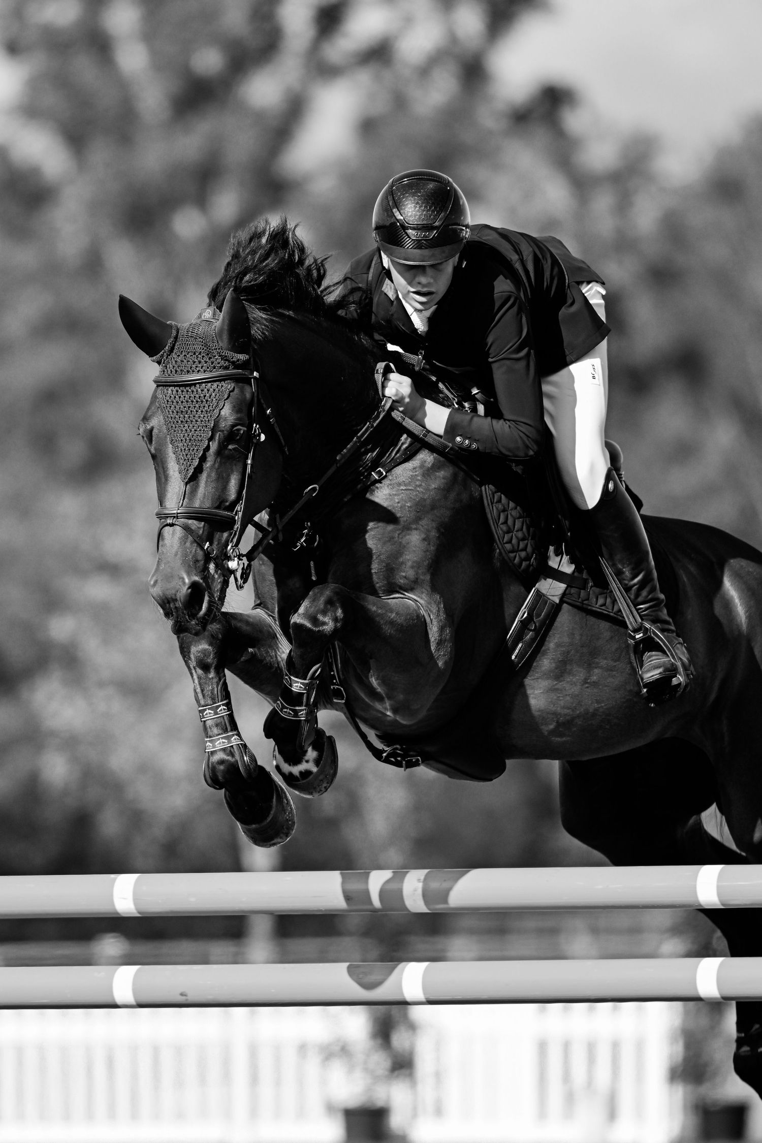 Black and white sequence of horse and rider jumping over competition barrier.