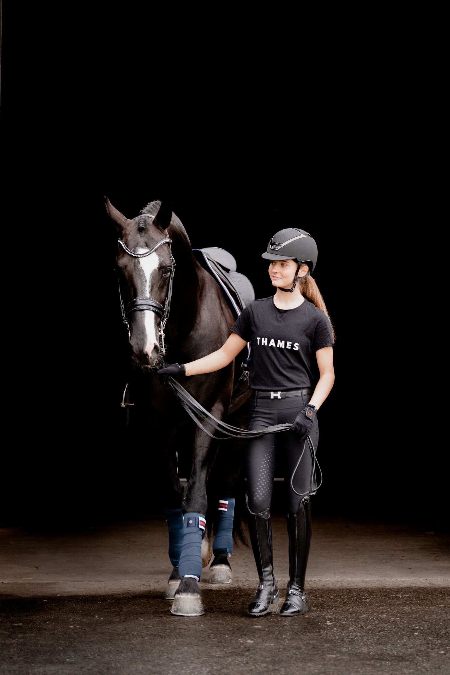 Black background photo of horse and rider walking towards the camera.