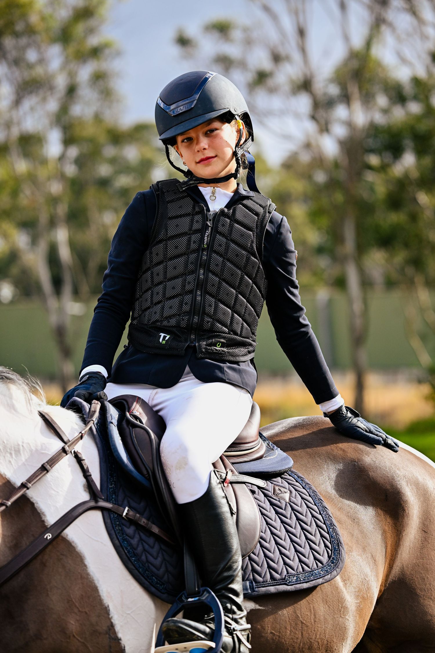 A rider in black protective gear sits atop a brown and white horse during an equestrian practice session.