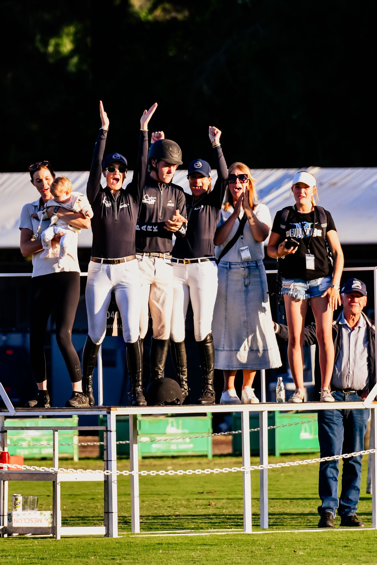 Spectators cheering and raising arms at an outdoor sports event.