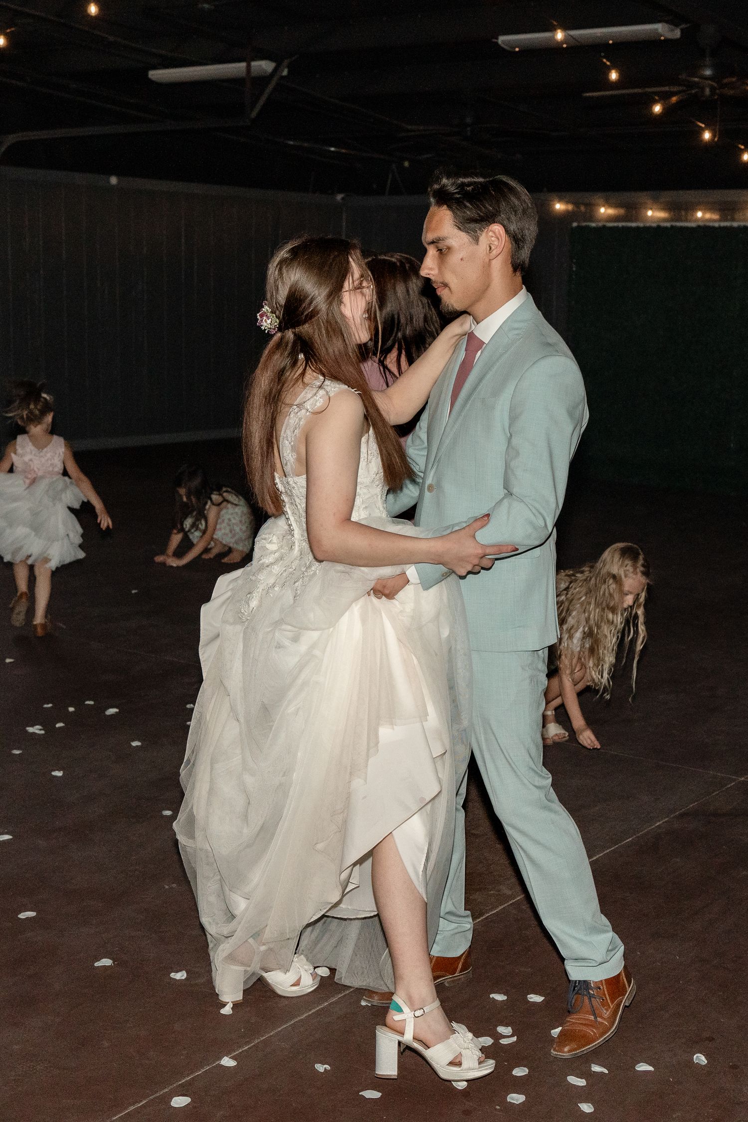 A couple dances together at a reception, with the bride wearing a flowing white dress and groom in light blue suit.