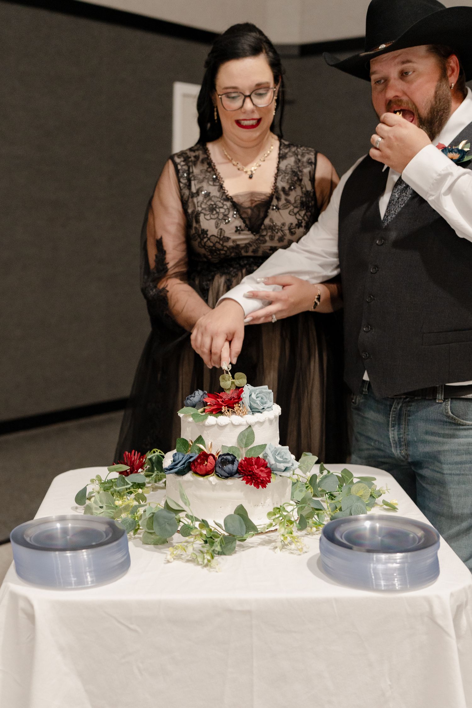 A couple cutting their white wedding cake decorated with fresh berries and greenery at their reception.