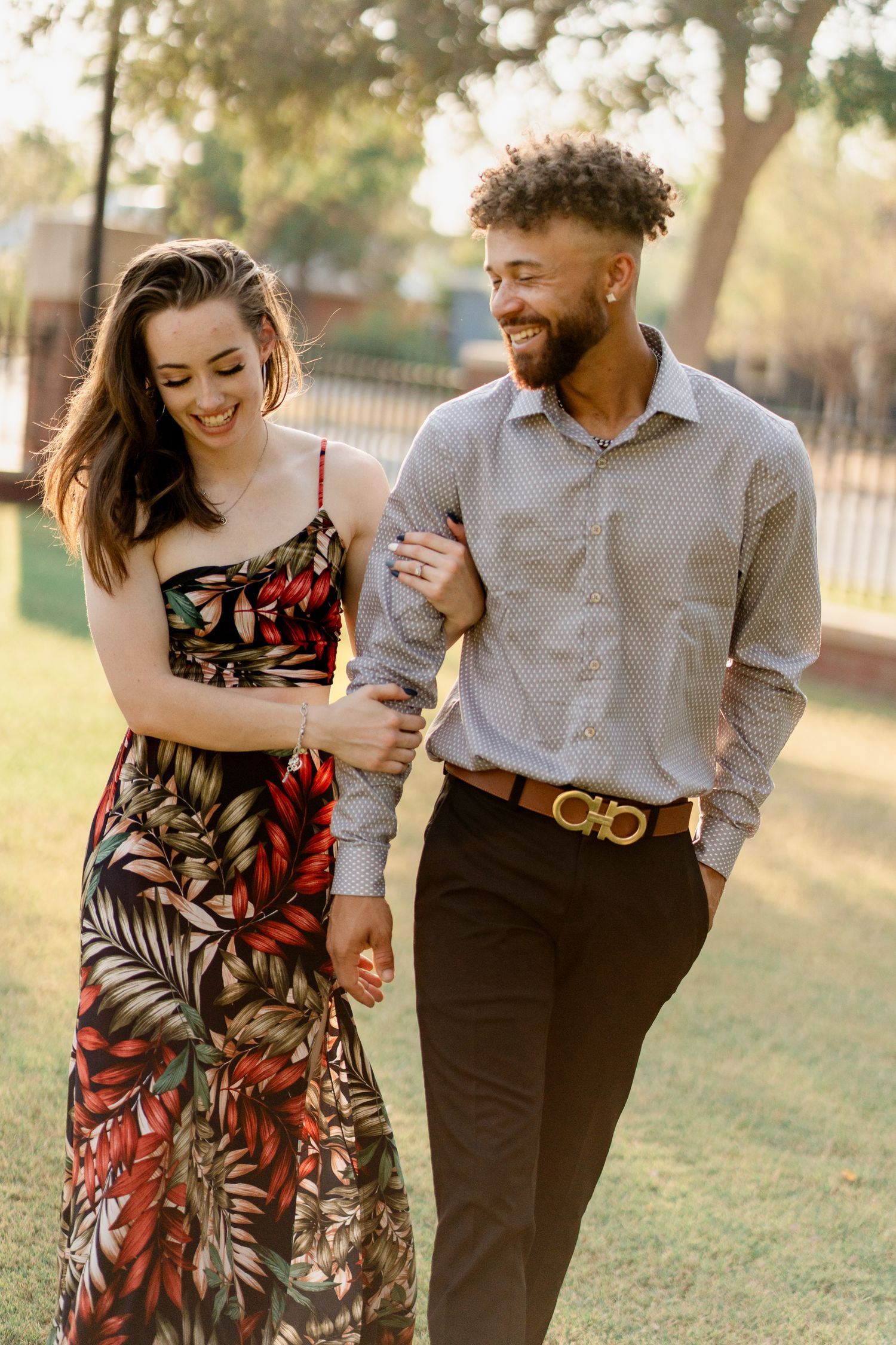A couple walks and laughs together during sunset in a park setting.