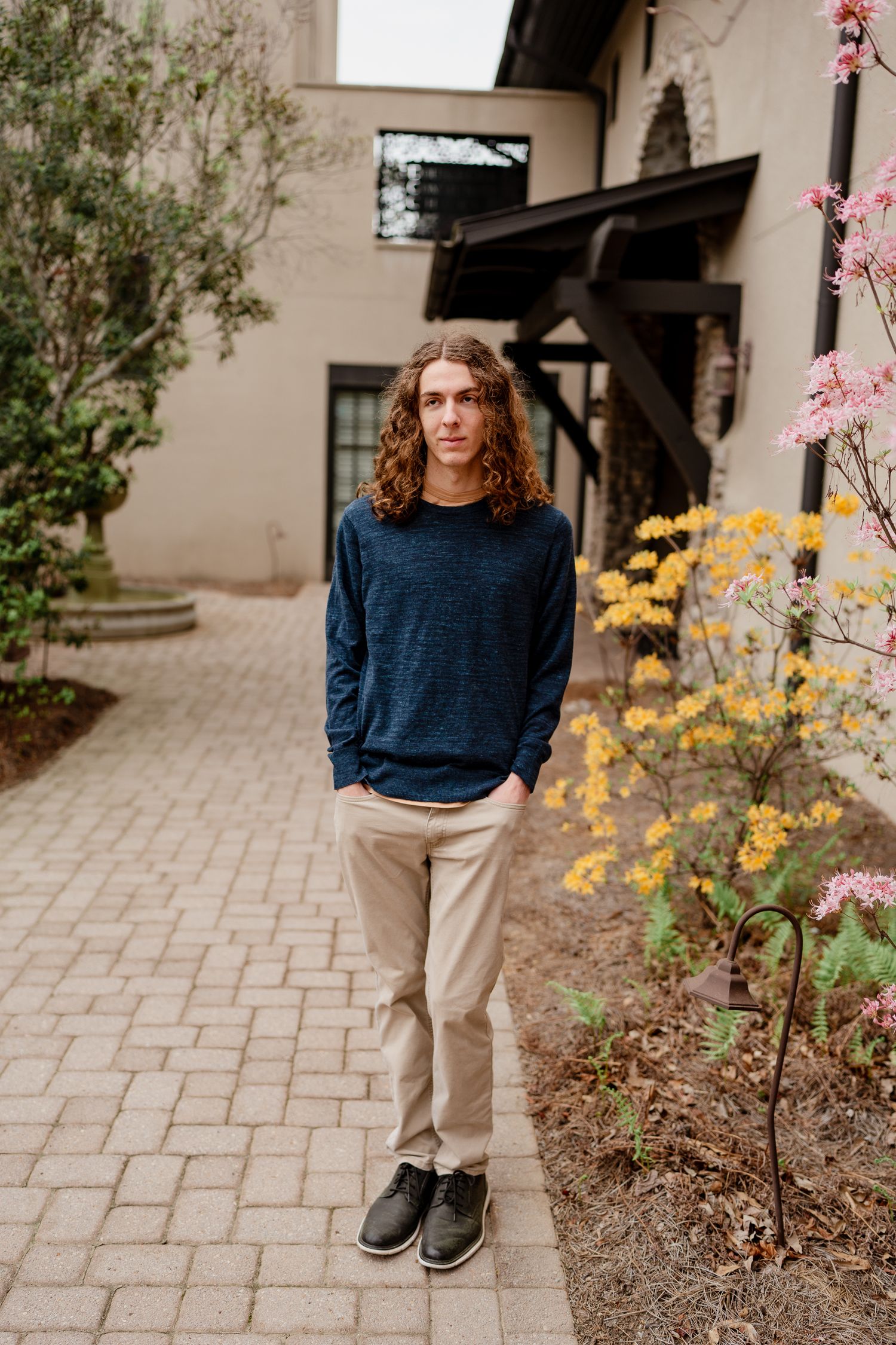Person in blue sweater and tan pants standing on paved path with spring flowers blooming.