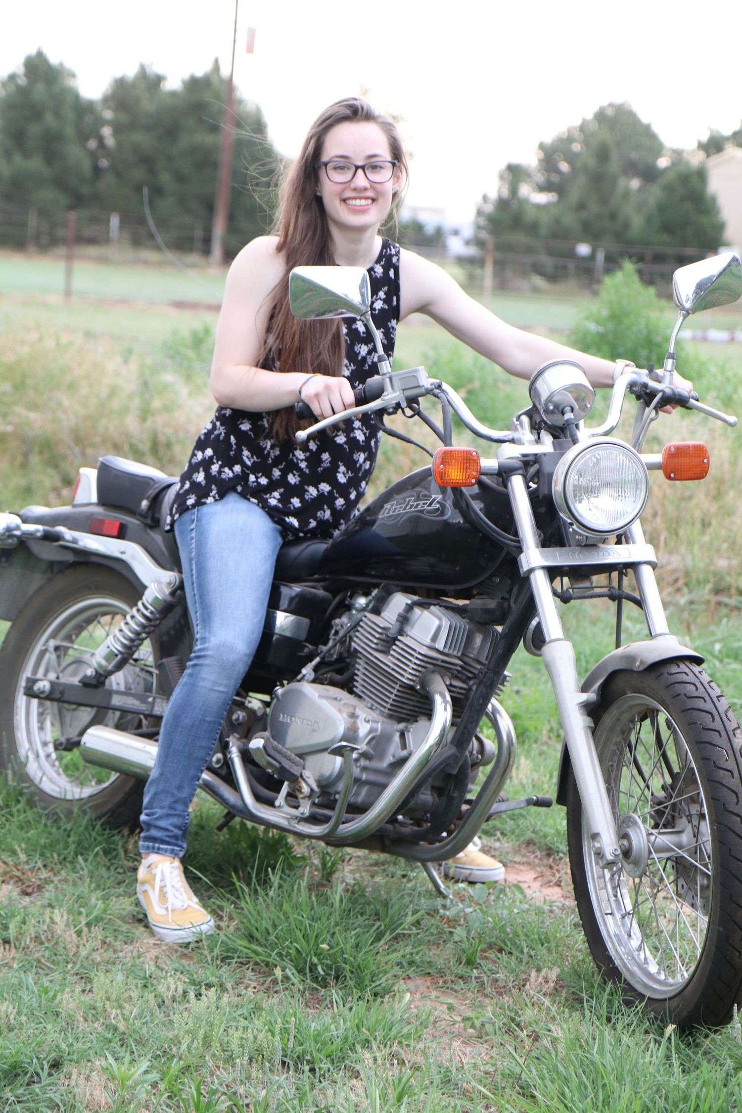 Vintage motorcycle enthusiast poses with classic bike in rural setting.