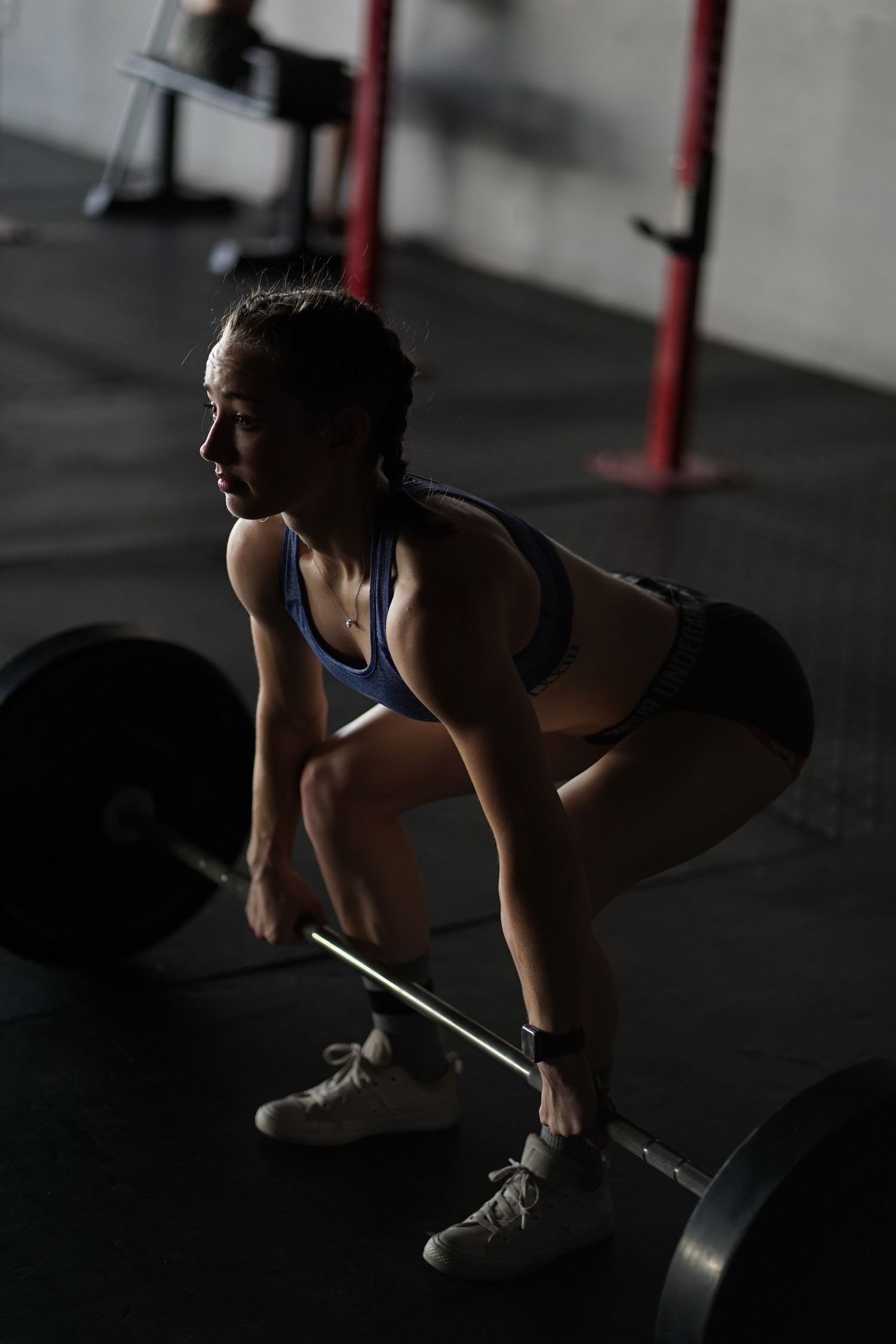 Athletic figure in blue sports attire performing deadlift exercise in dark gym setting.