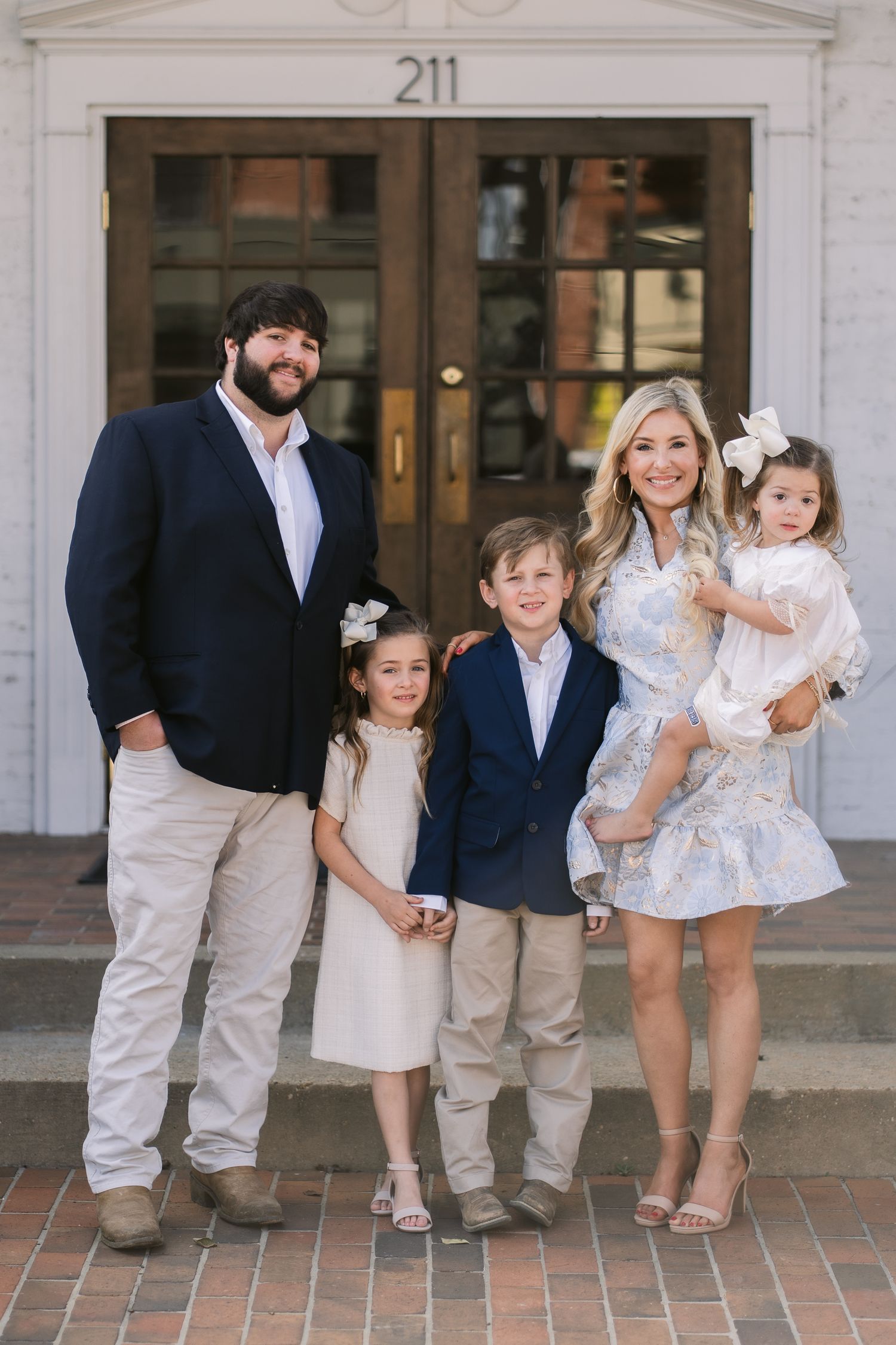Family portrait showing adults and children in coordinated white and navy outfits standing on a brick walkway.
