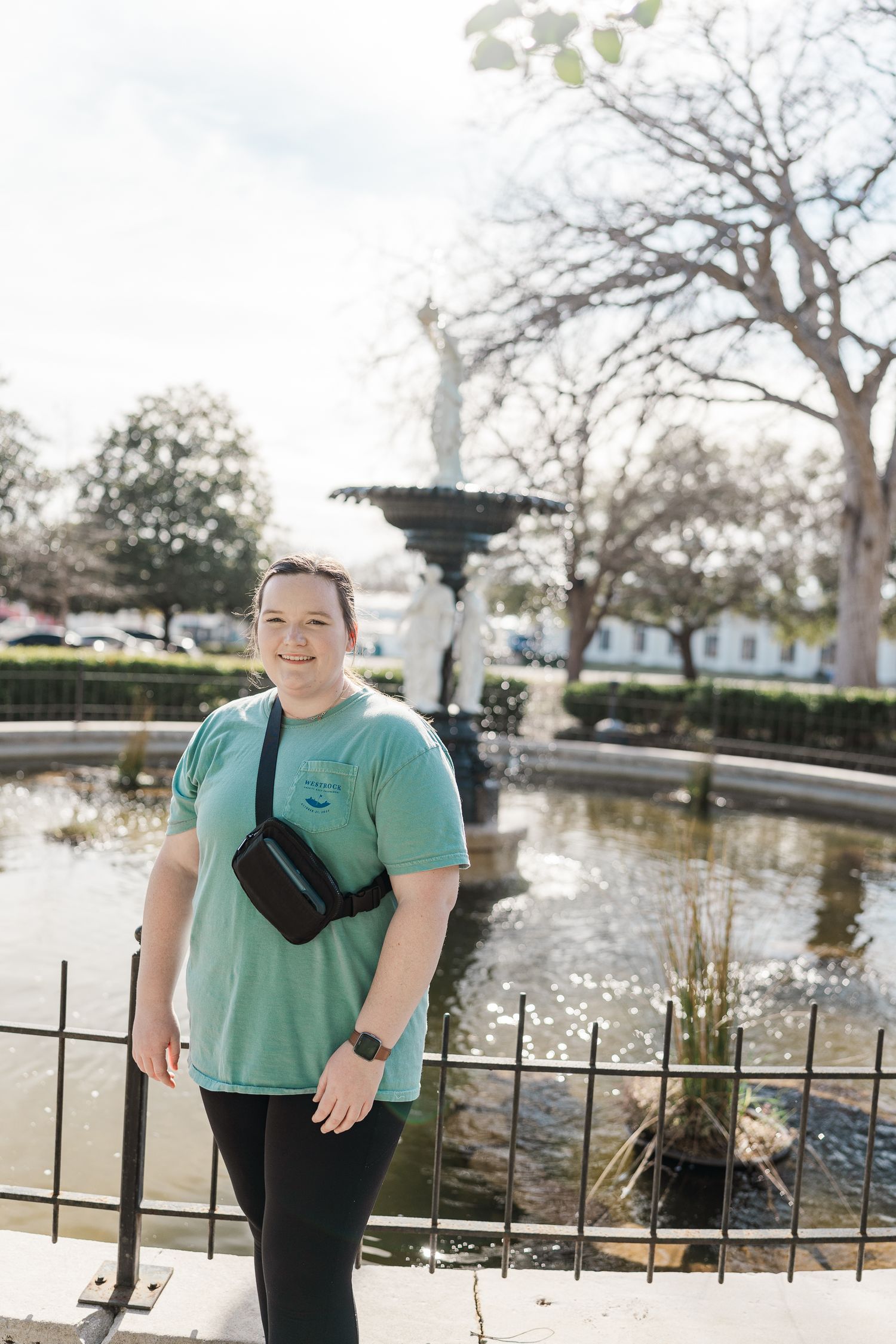 Person standing by ornate fountain in sunny park setting.