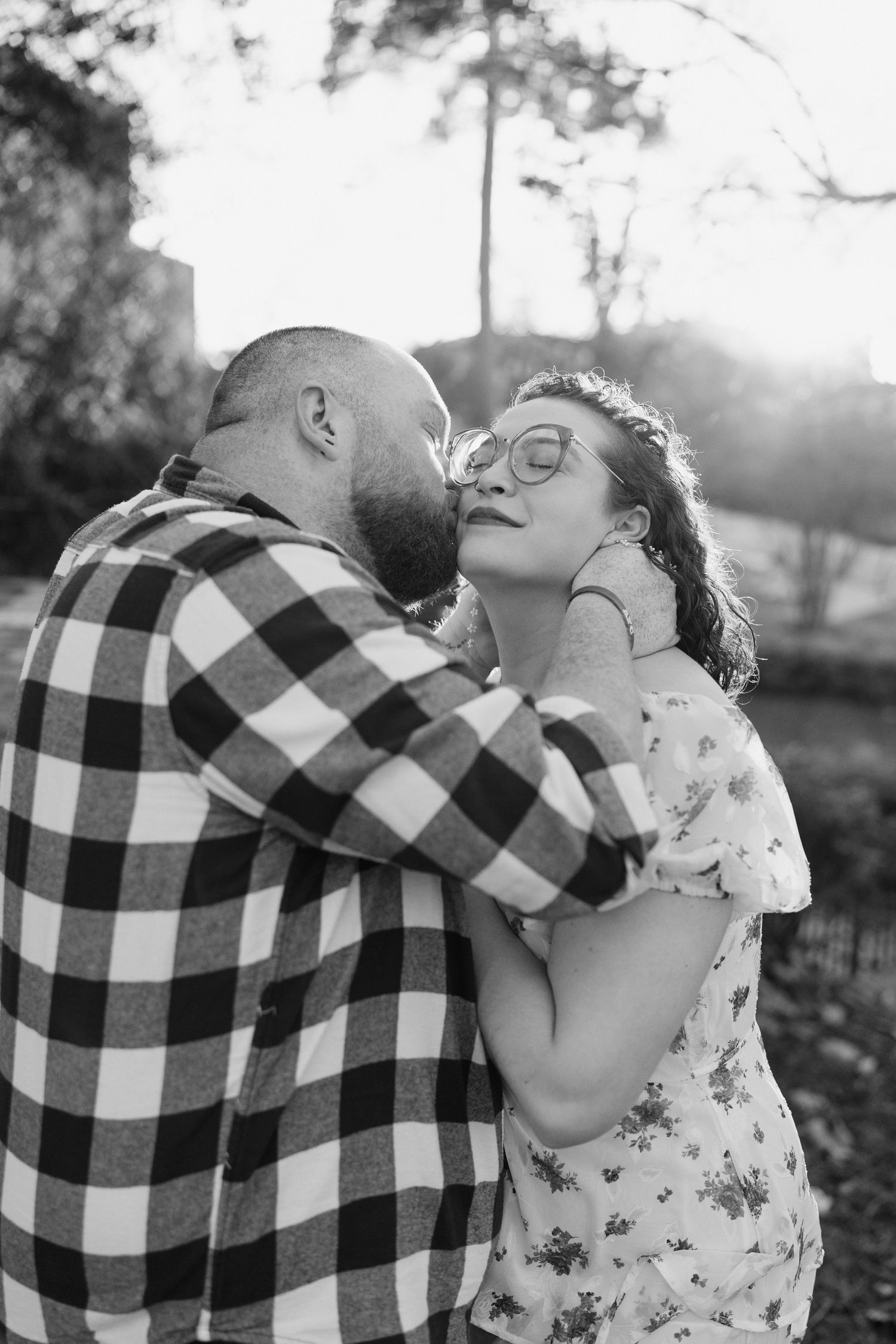 A romantic couple in buffalo plaid and floral attire share tender moments in a black and white photo series.
