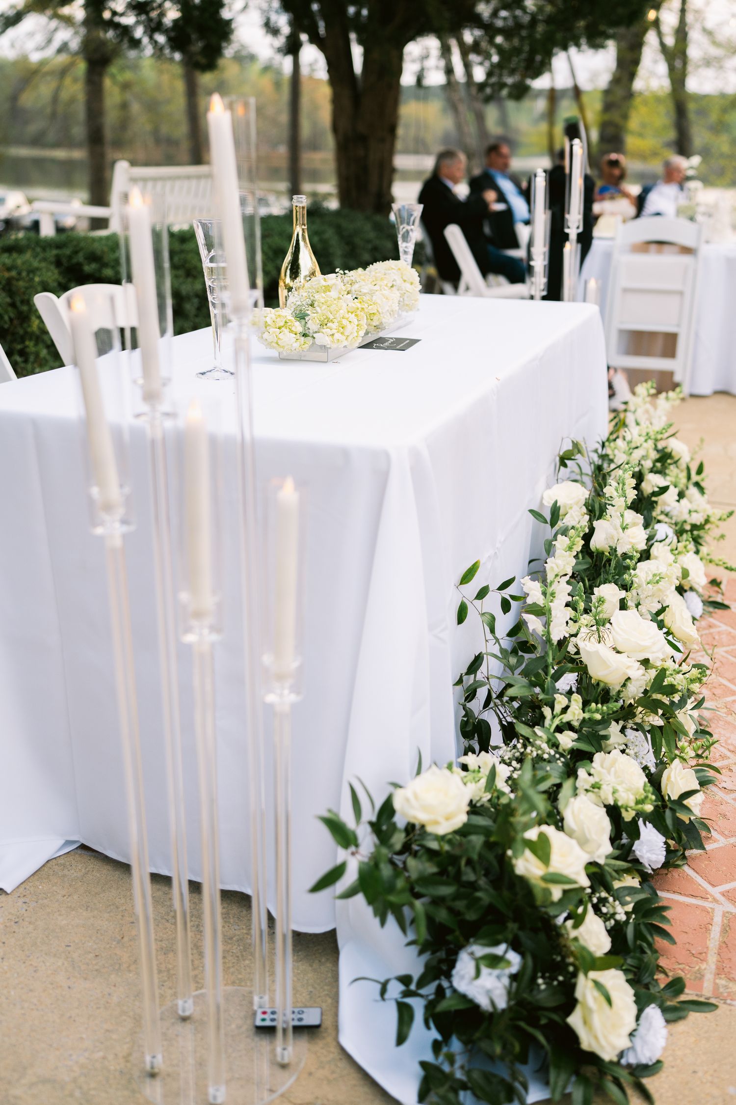 Elegant wedding table setting with white linens, tall candles and white floral arrangements.